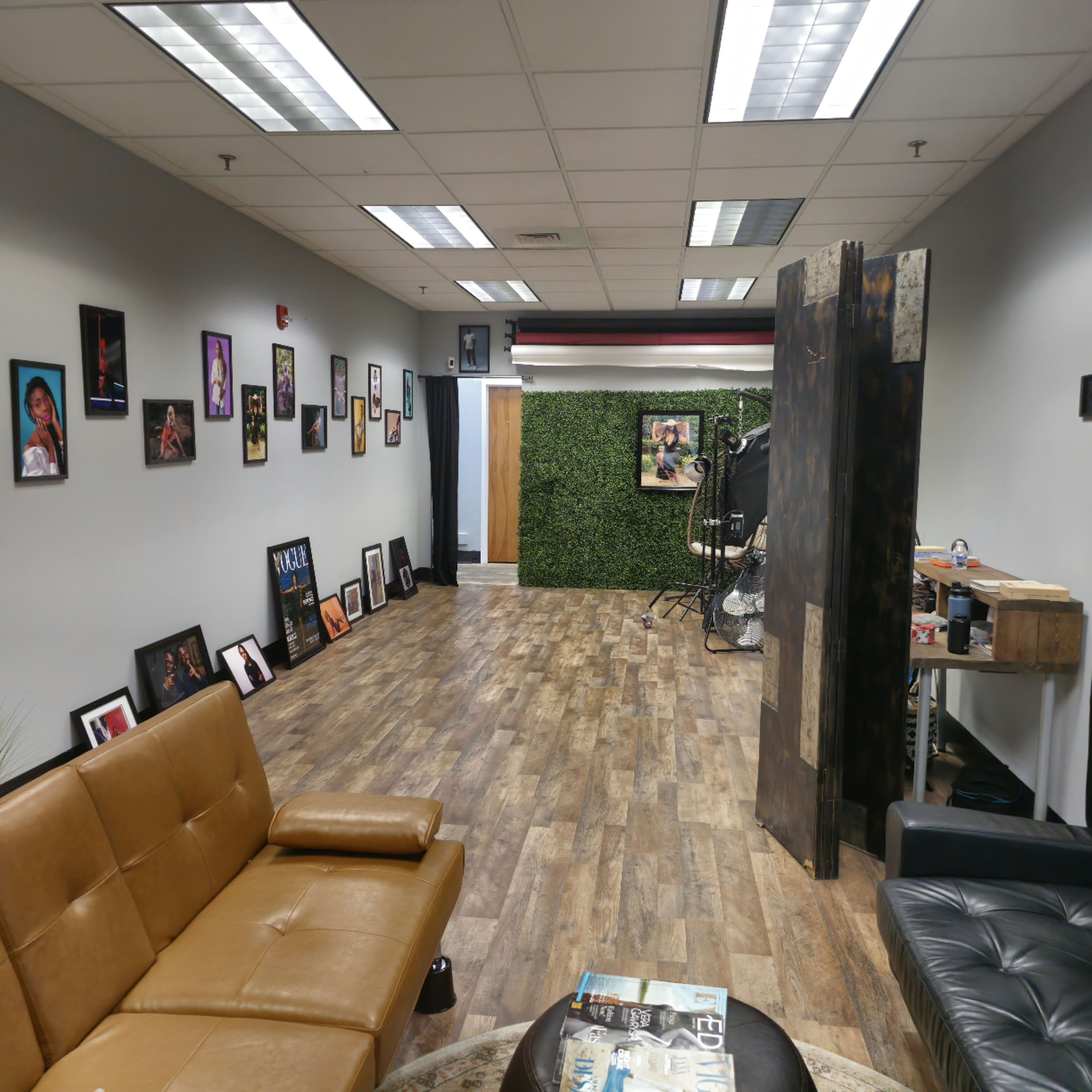 A hallway in a studio or office space, featuring framed photos on the walls, a brown leather sofa, and a green wall separating a workspace.