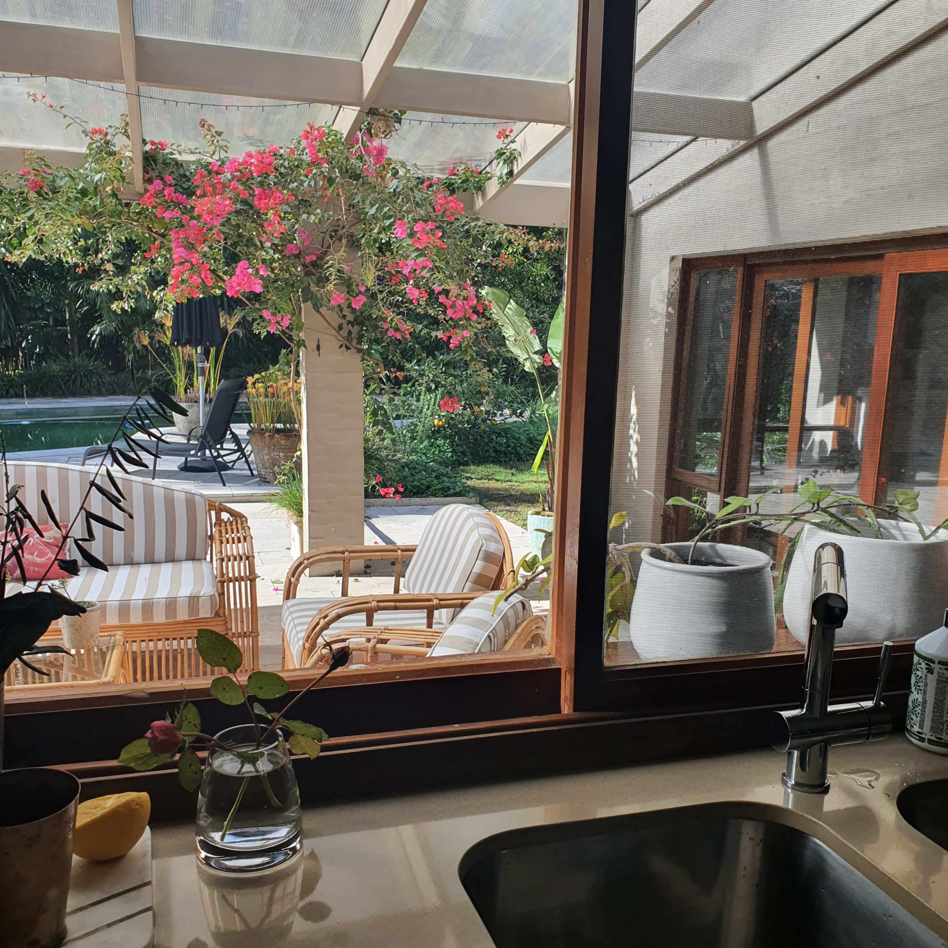 A kitchen sink with a view of a patio area filled with potted plants and outdoor furniture.