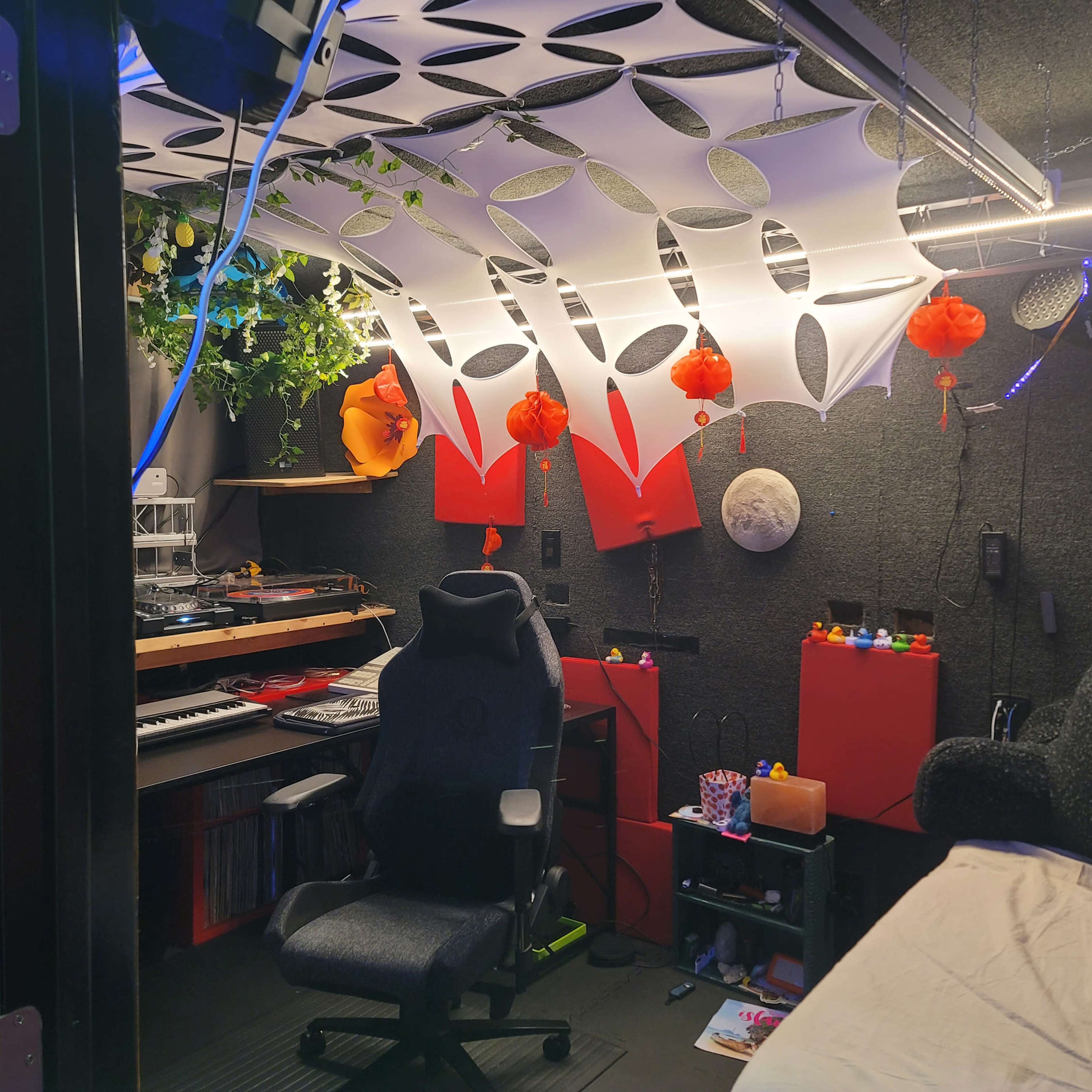A small music studio features a computer desk with equipment, colorful decorations, and a comfortable chair.