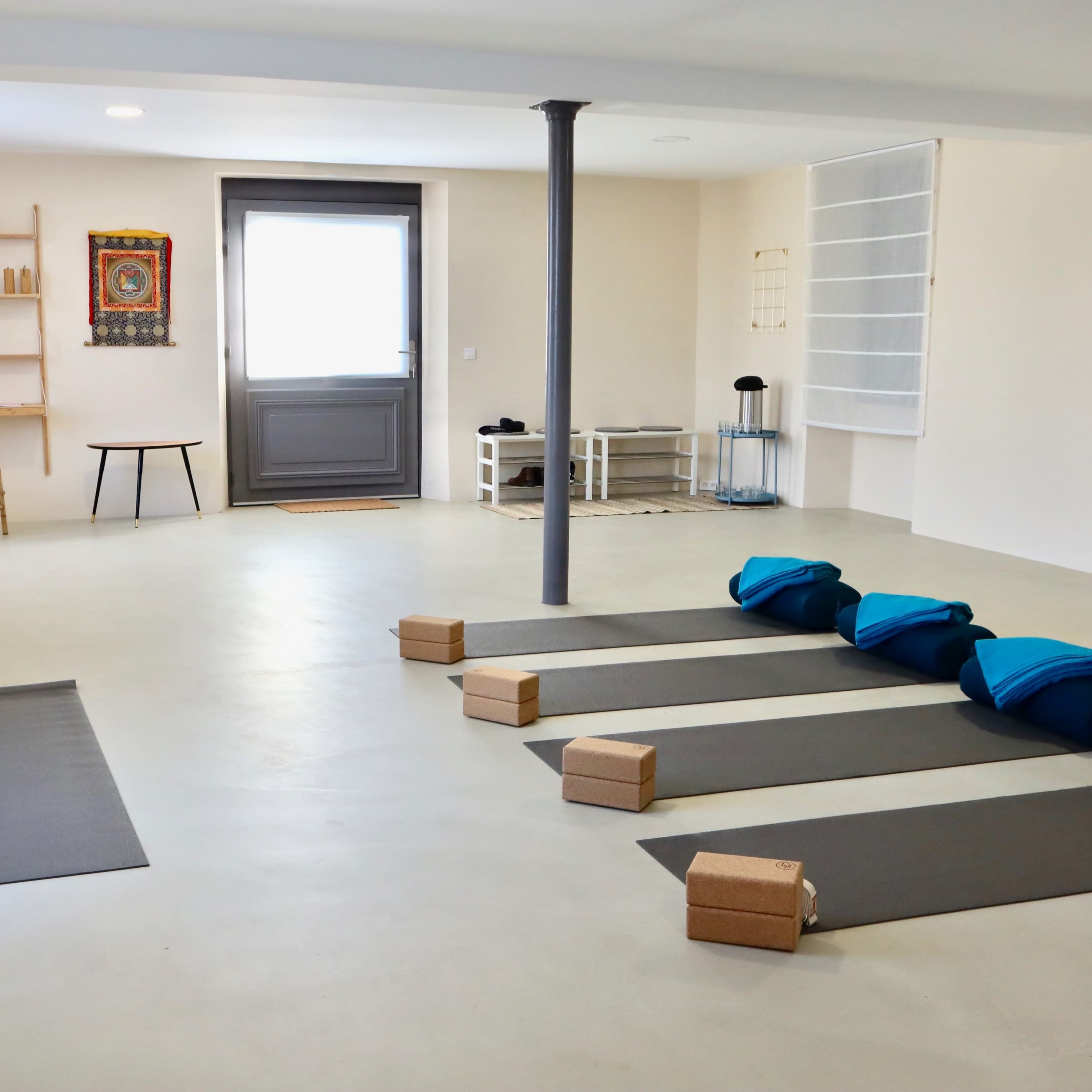 A spacious, minimalistic yoga studio featuring exercise mats, blocks, and a few pieces of furniture.