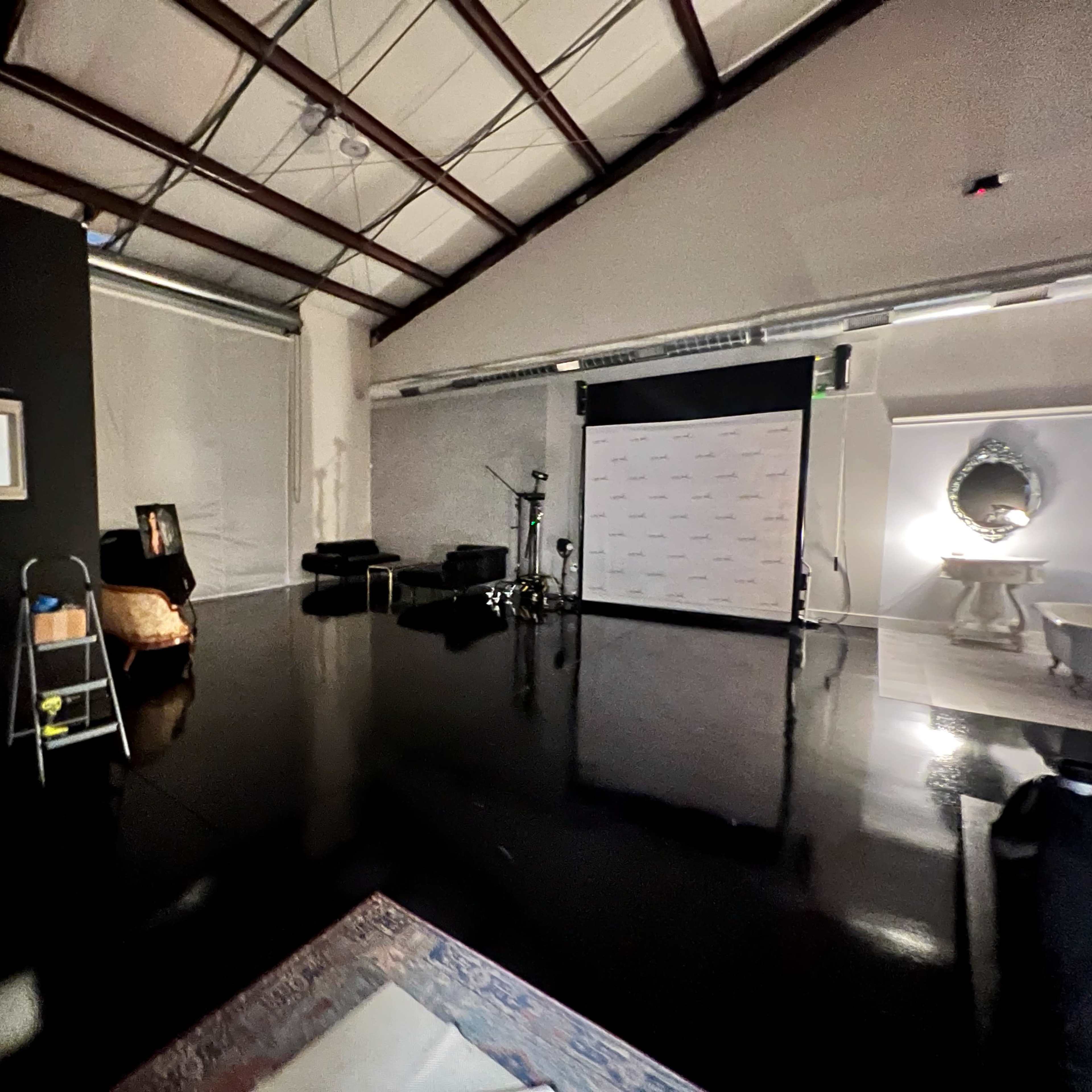 An industrial-style studio with polished black floors, a backdrop for photography, and various furnishings including a chair and a large mirror.