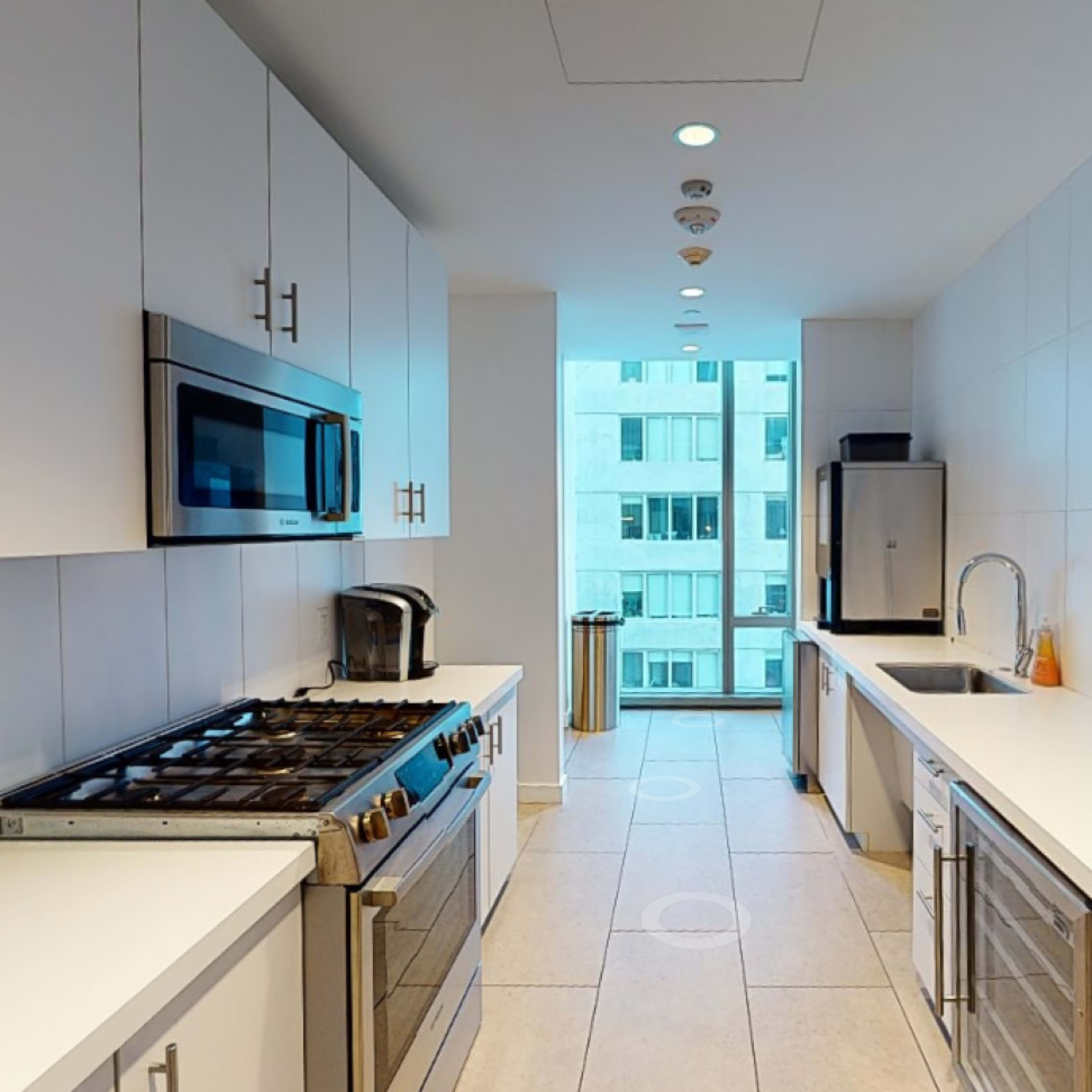 A modern kitchen with white cabinetry, stainless steel appliances, and large windows allowing natural light.