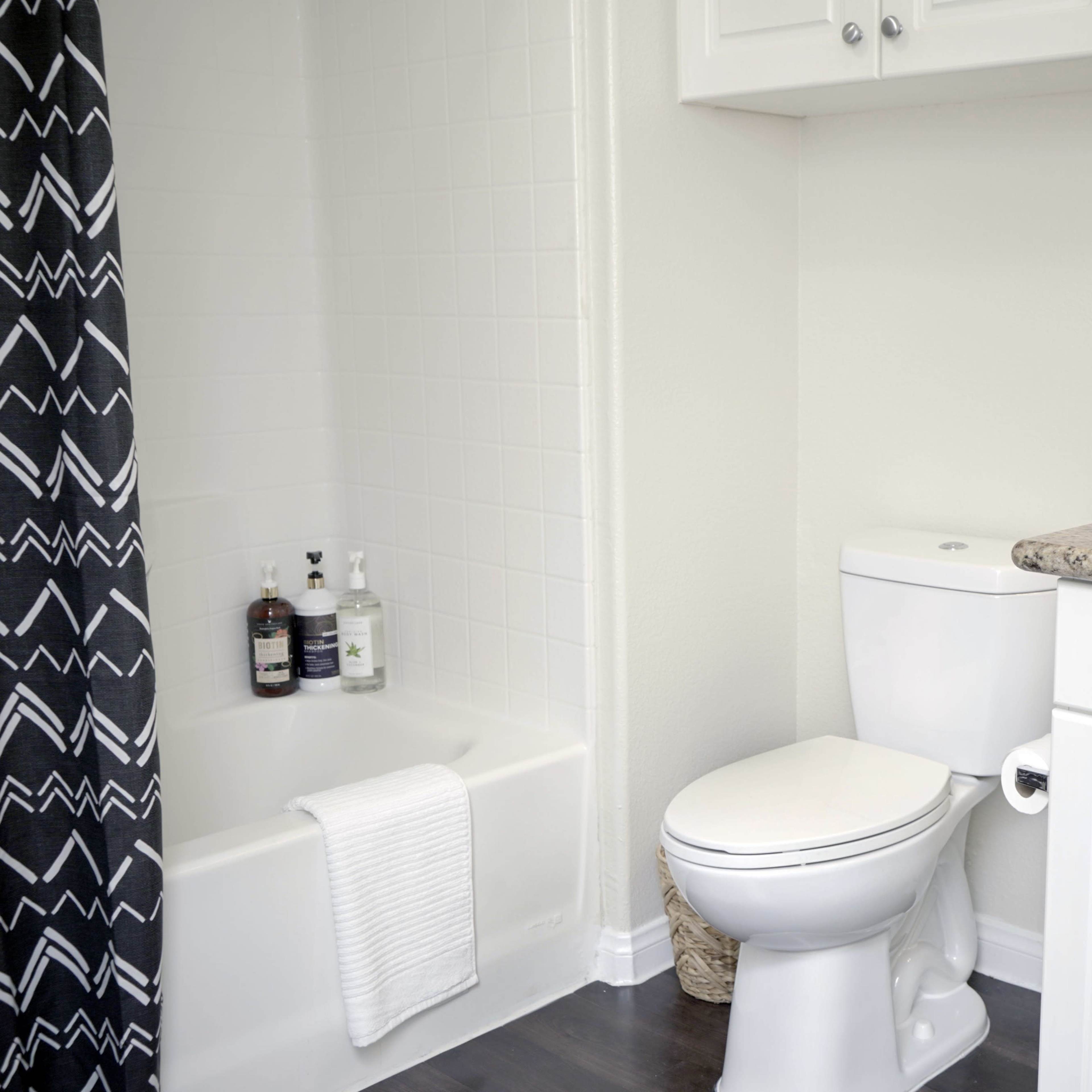 A clean bathroom featuring a bathtub with toiletries, a white toilet, and a granite countertop with a sink.
