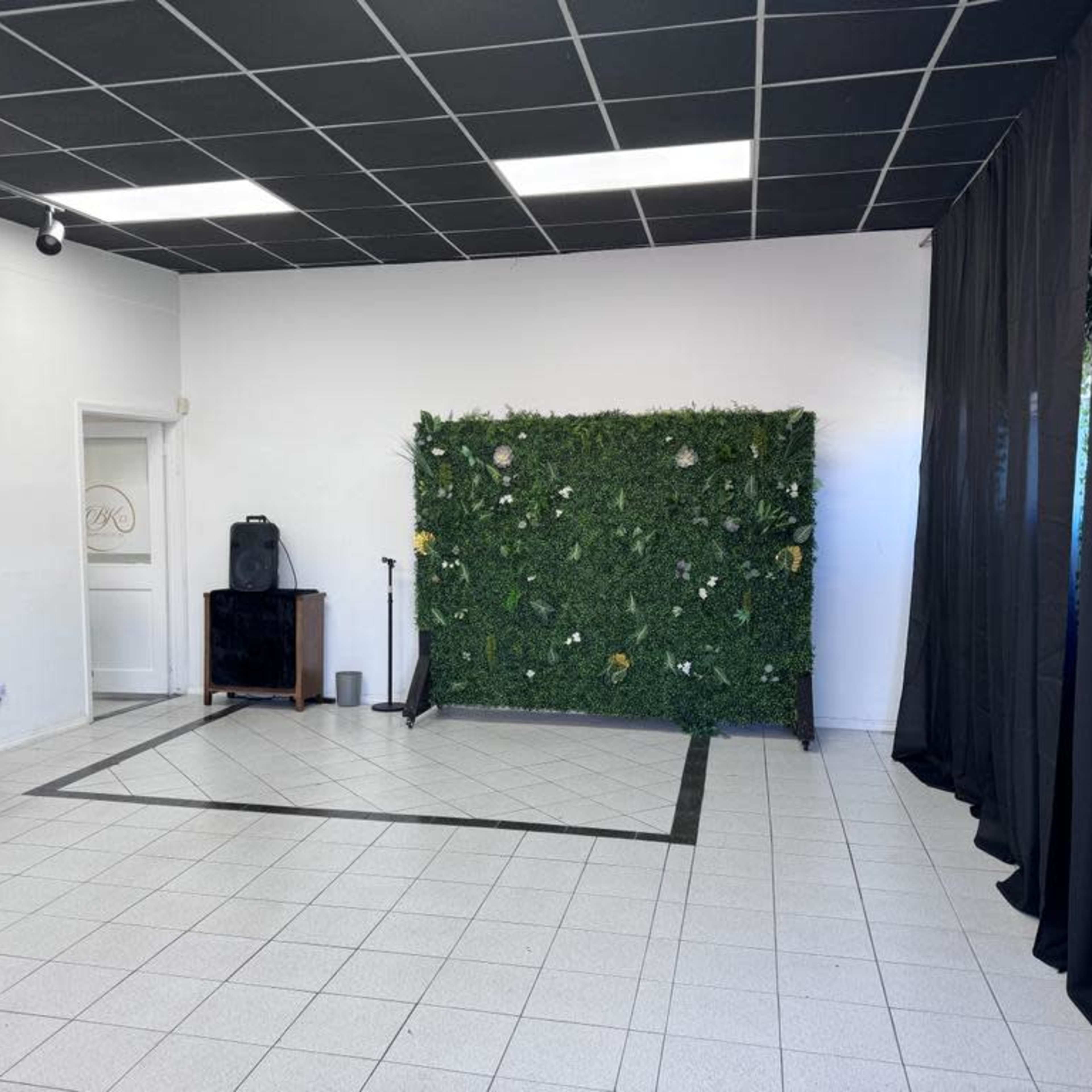 An empty room with a tiled floor, a green plant wall on one side, and black curtains along another wall.