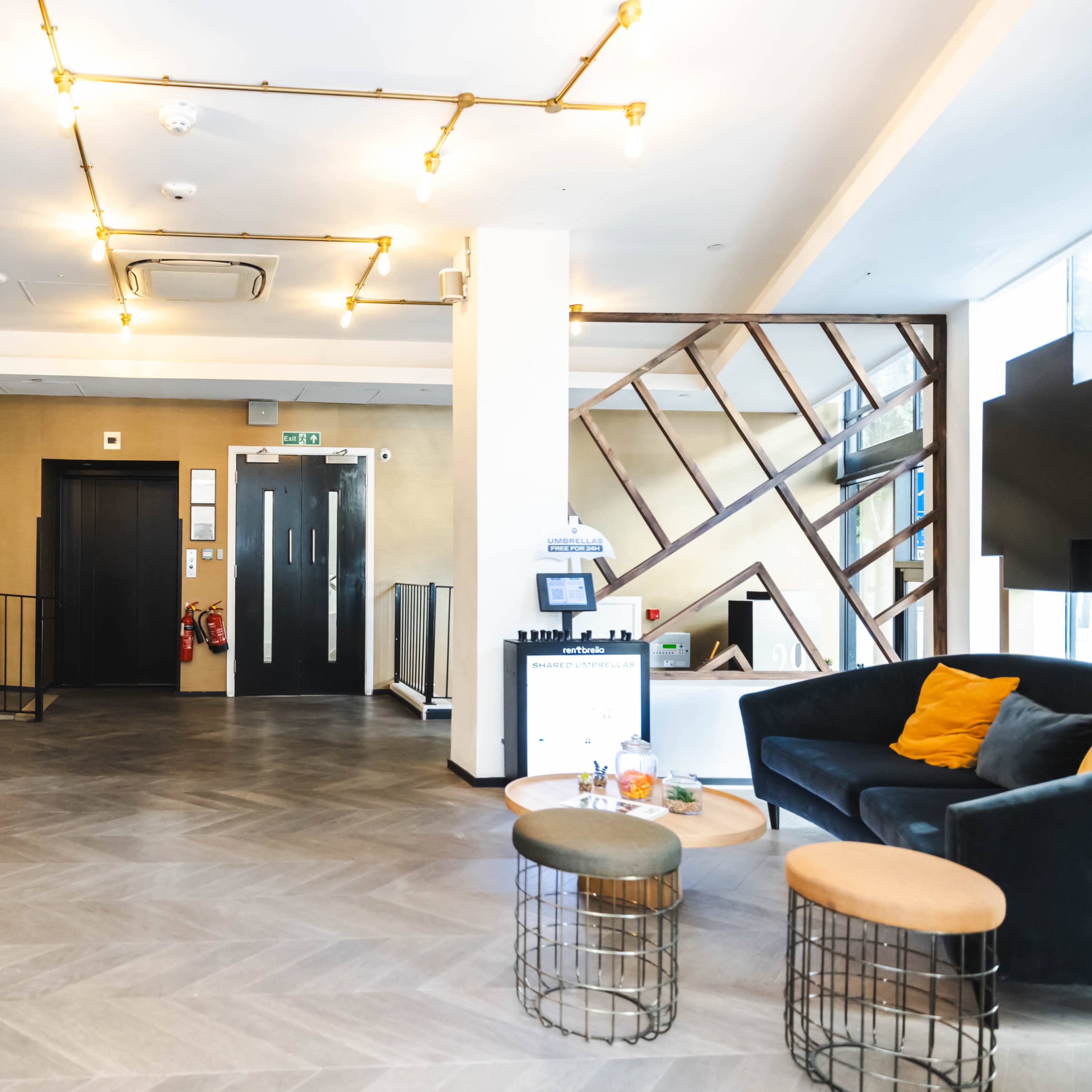 A modern reception area with a dark sofa, a wooden reception desk, and decorative lighting fixtures.
