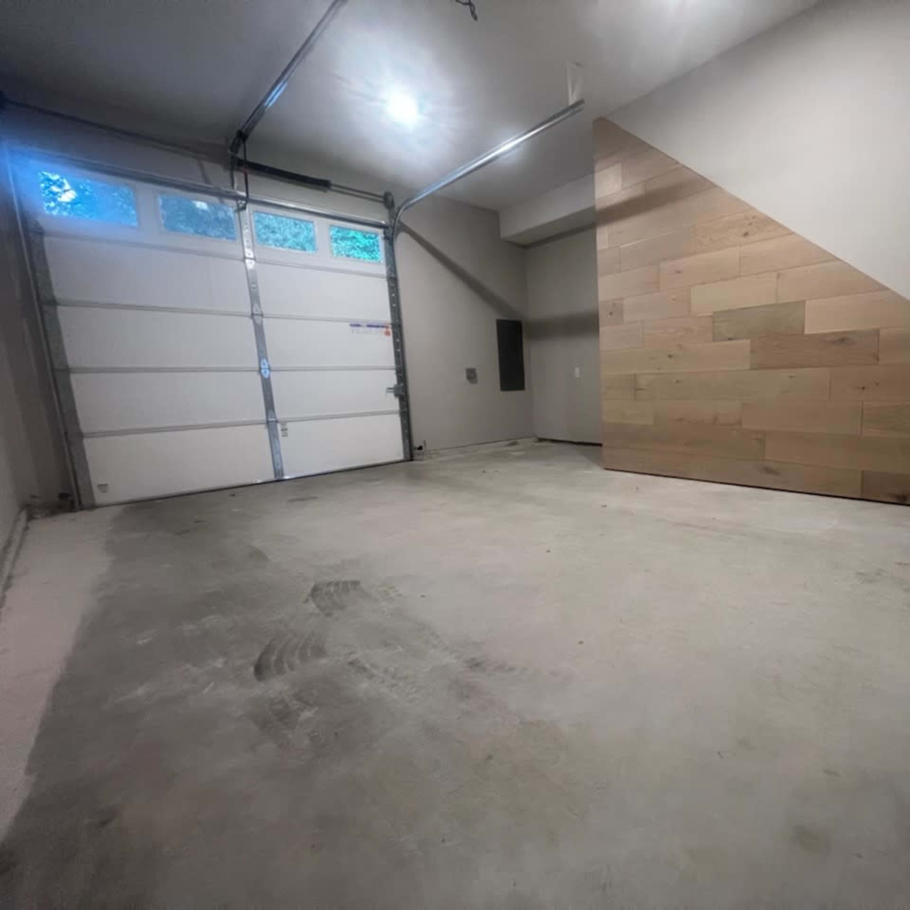 An empty garage with a concrete floor and a wooden accent wall on one side.