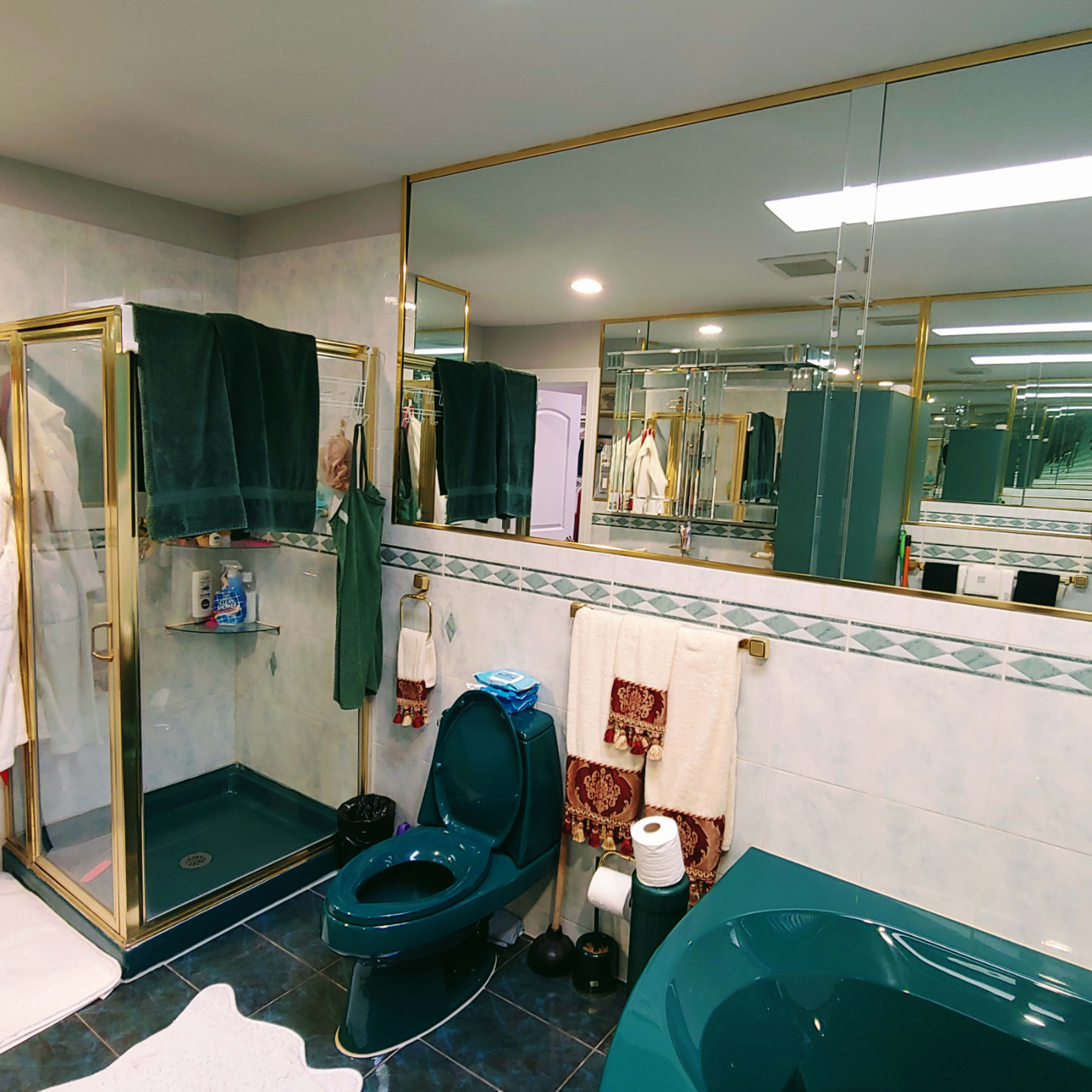 A bathroom features a glass shower stall, a toilet, and a double sink, with towels hanging and mirrors reflecting the space.