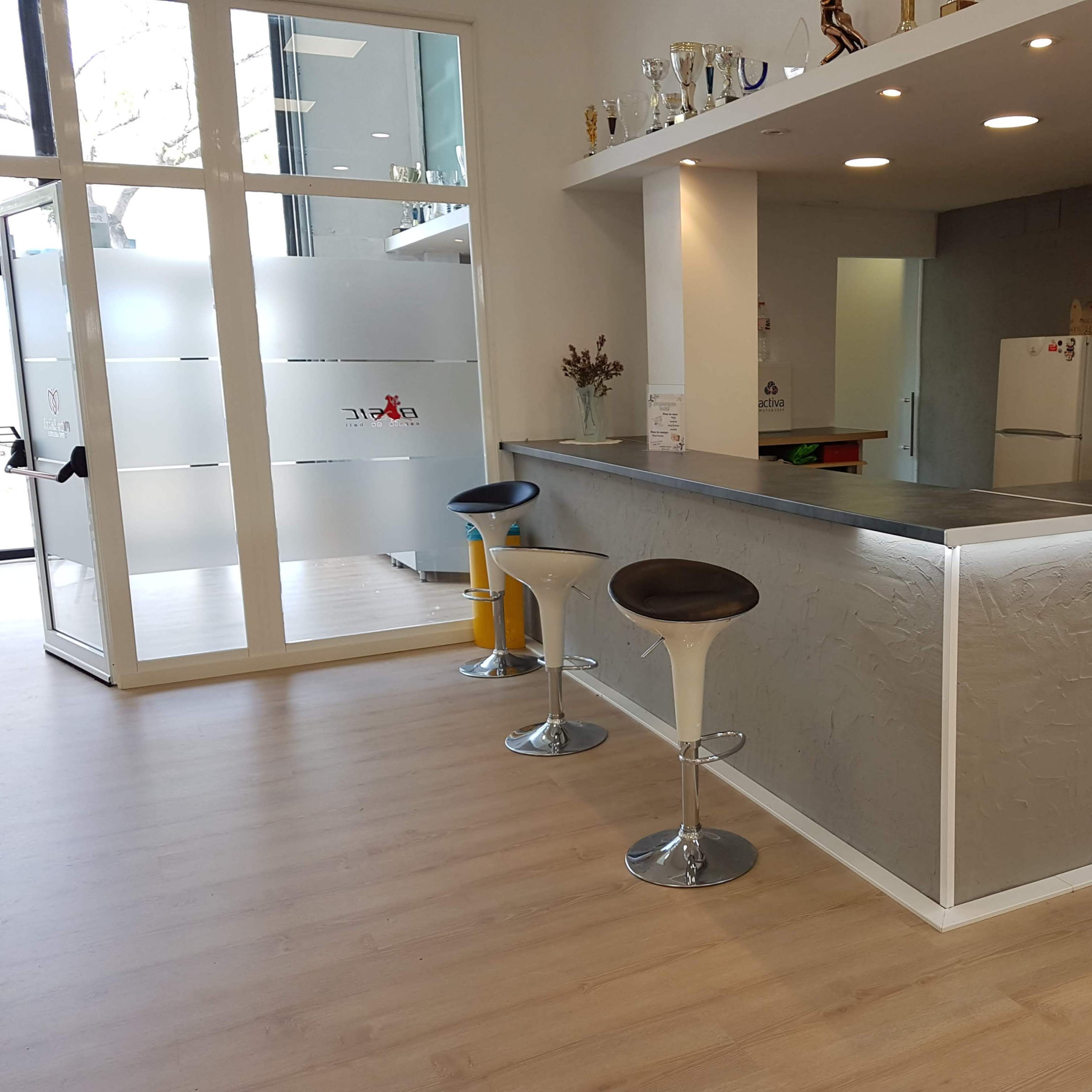 A modern interior space featuring a counter with bar stools, a kitchen area, and a large window with frosted glass.
