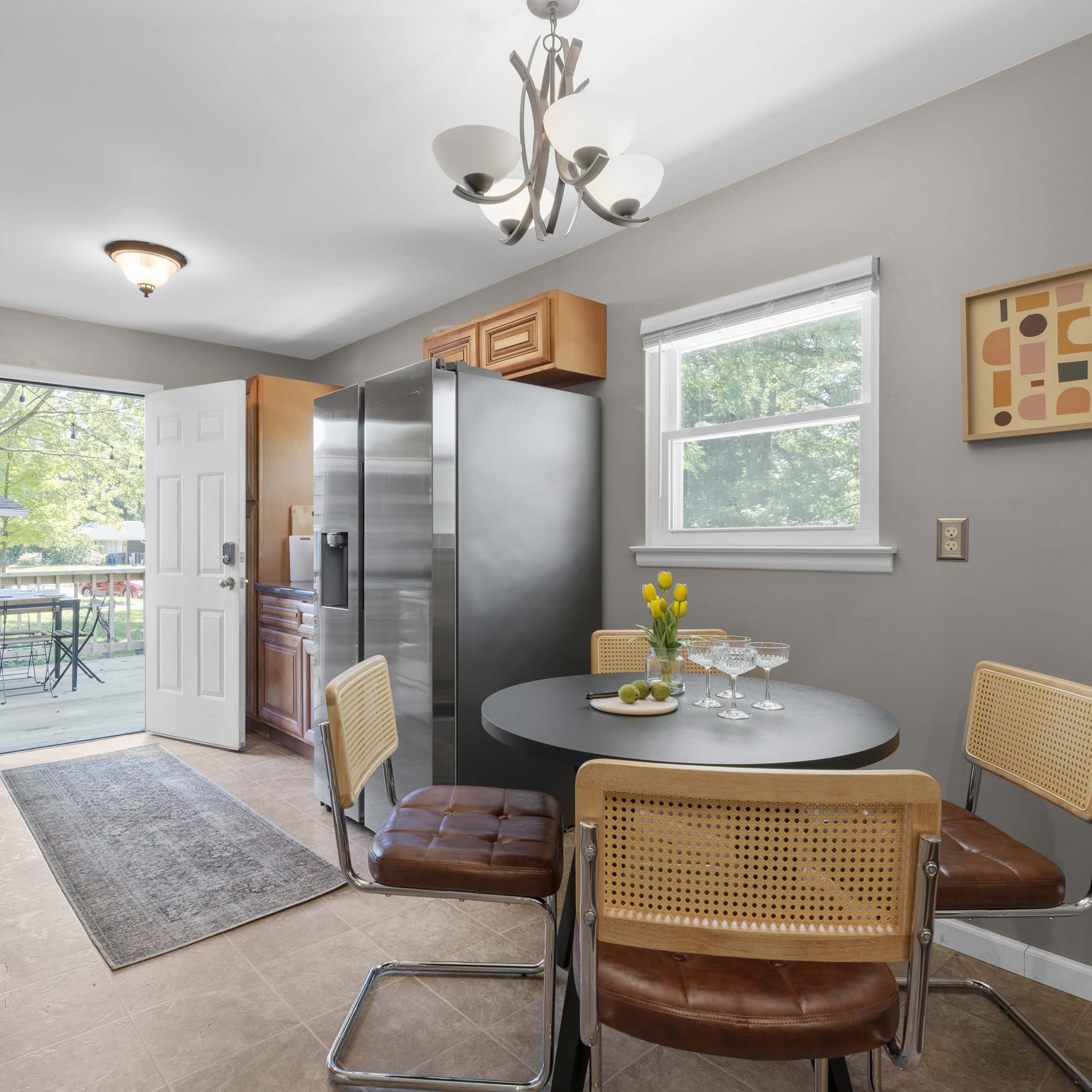 A modern kitchen features a circular table with four chairs, a stainless steel refrigerator, and a door leading to an outdoor area.