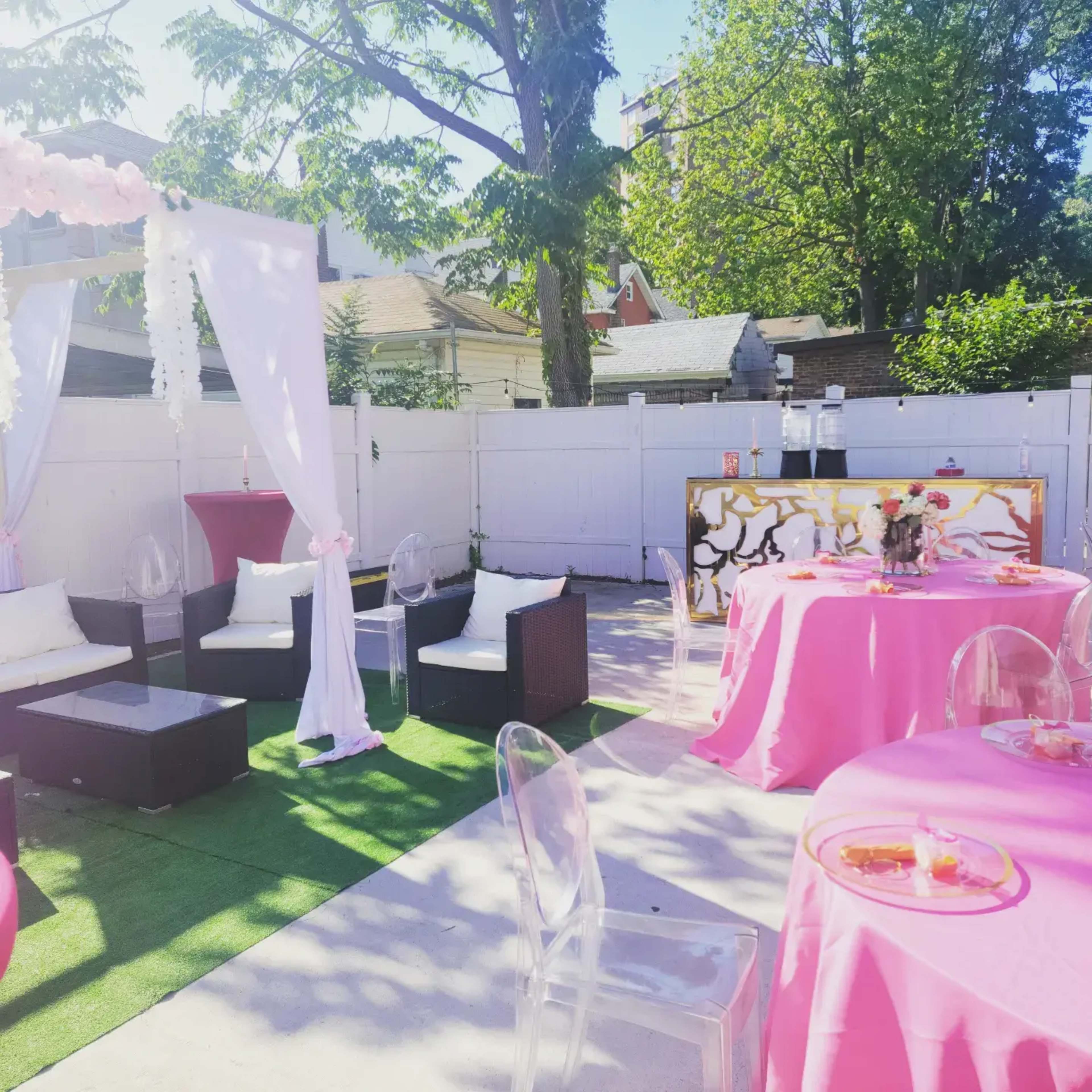 The scene features an outdoor party setup with pink tables, clear chairs, a decorated canopy, and greenery surrounding the space.