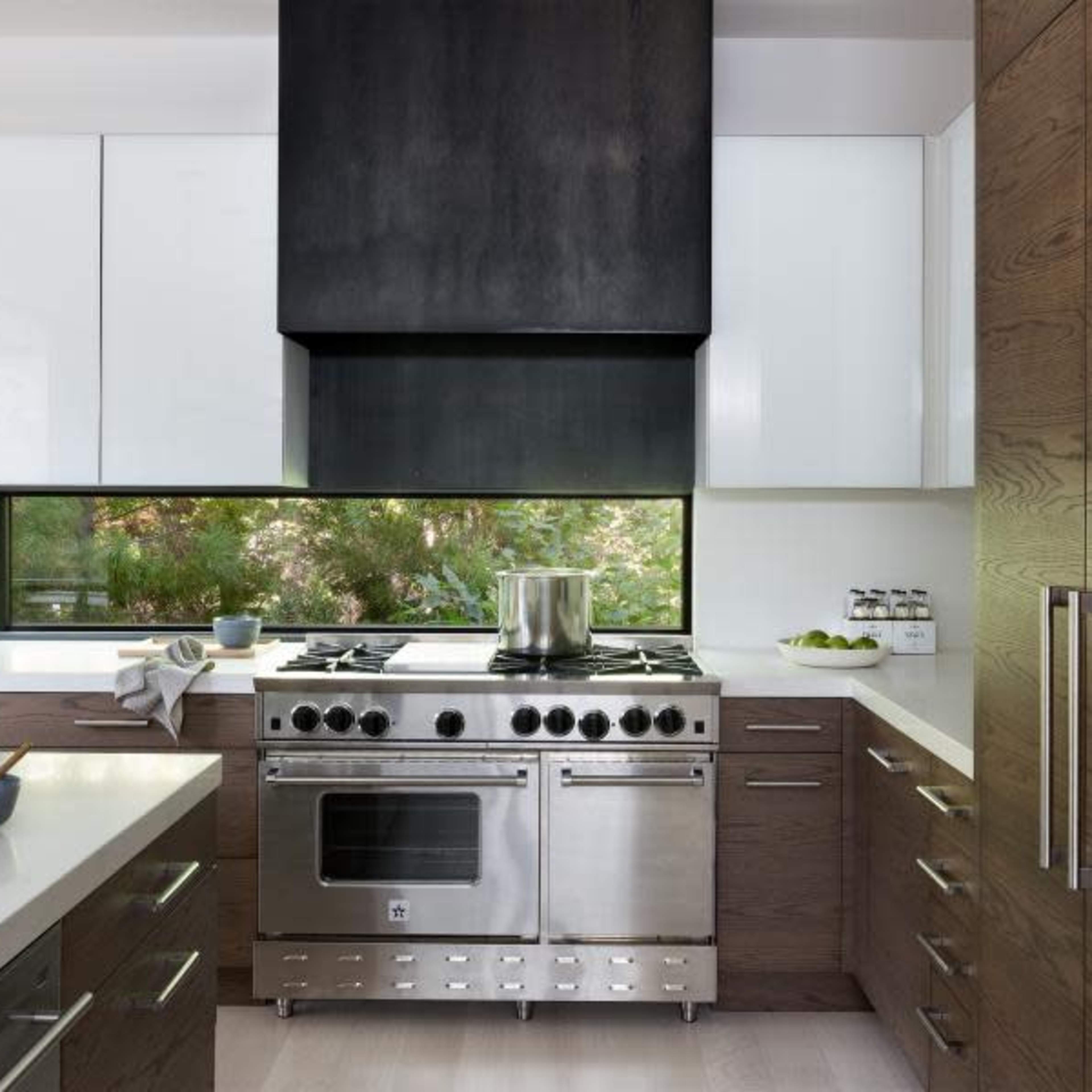The kitchen features a stainless steel stove under a black hood, with white and dark wood cabinetry and a window providing natural light.