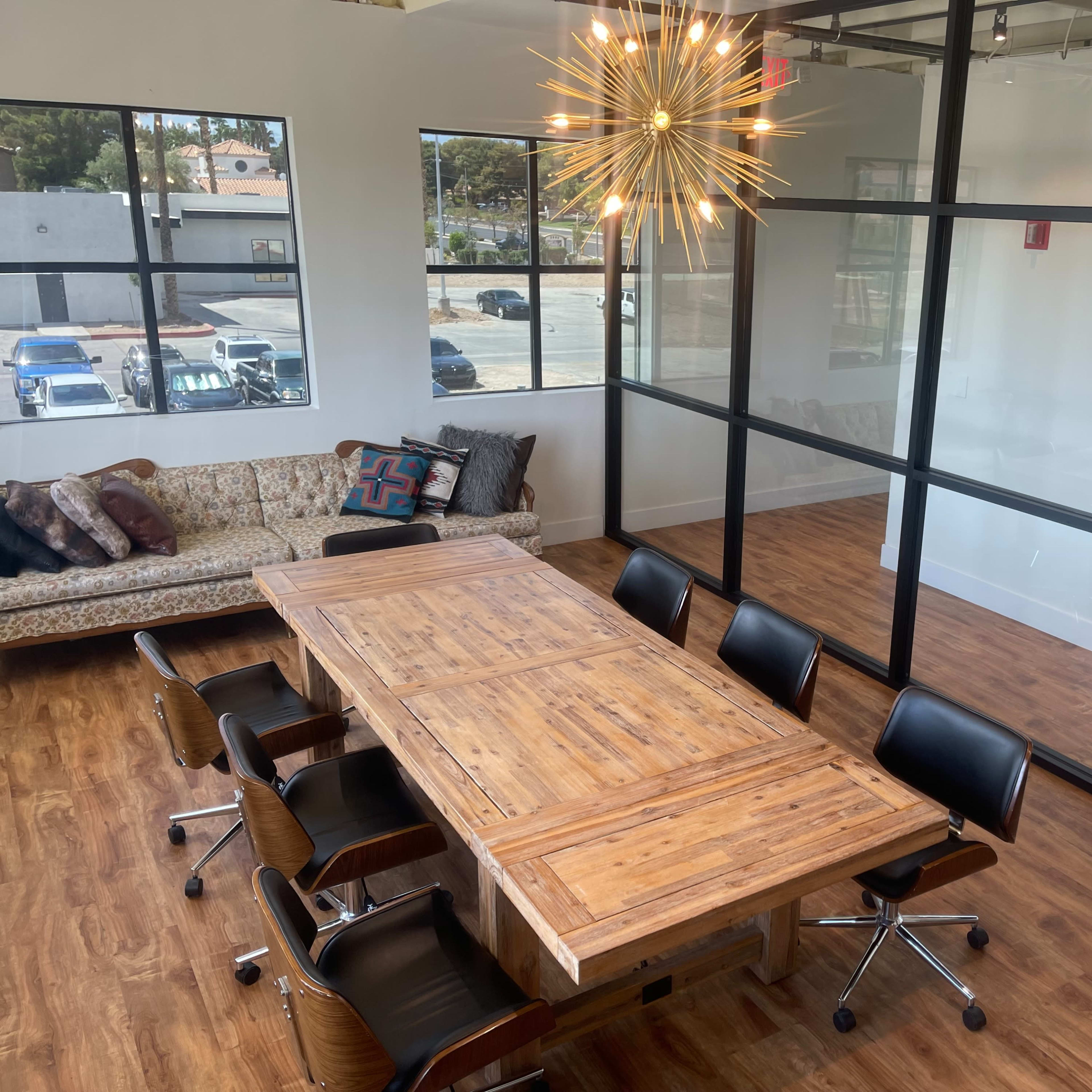 A modern conference room with a large wooden table surrounded by black chairs and a decorative light fixture overhead.