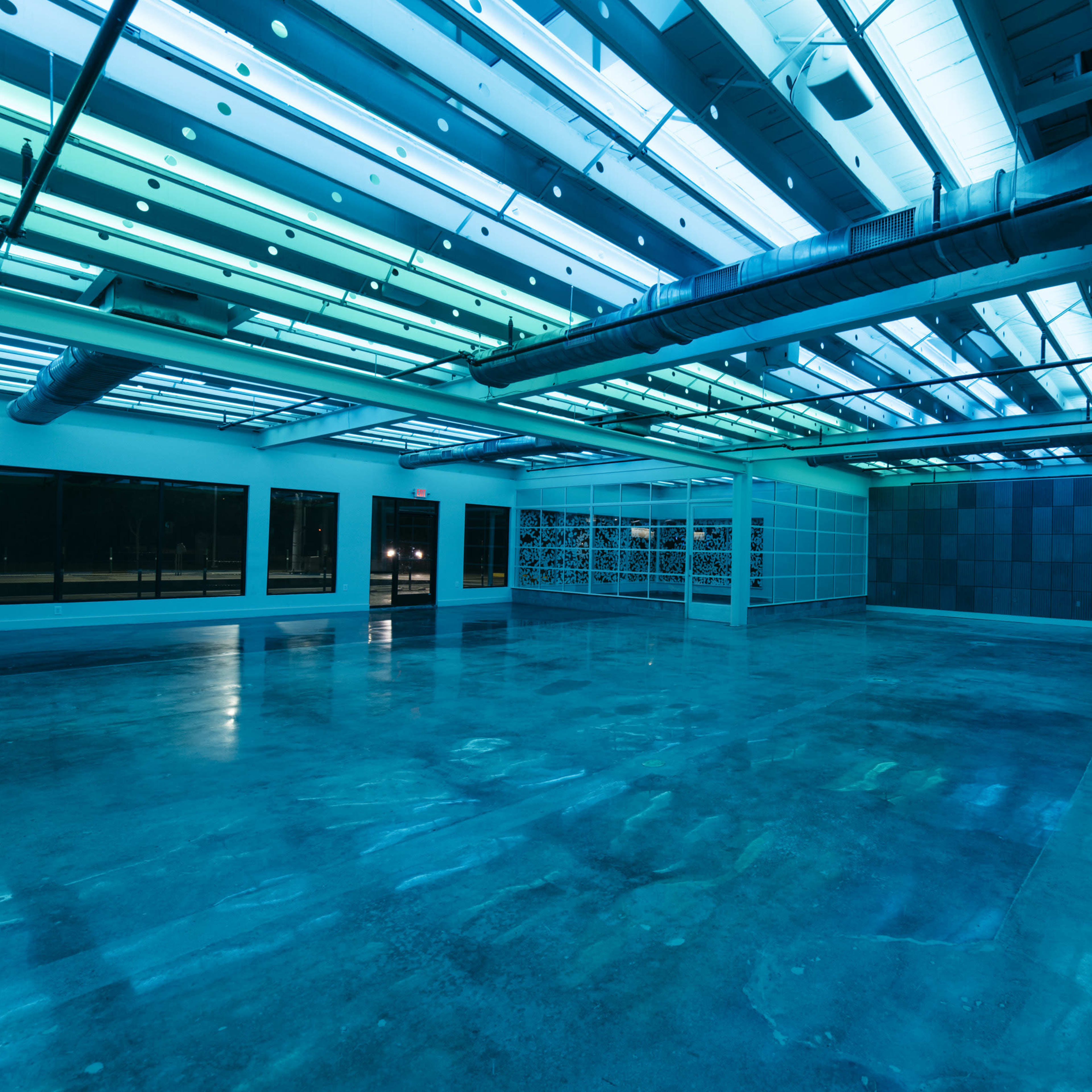 A large, empty room with polished concrete floors and overhead lights casting a blue-green glow.