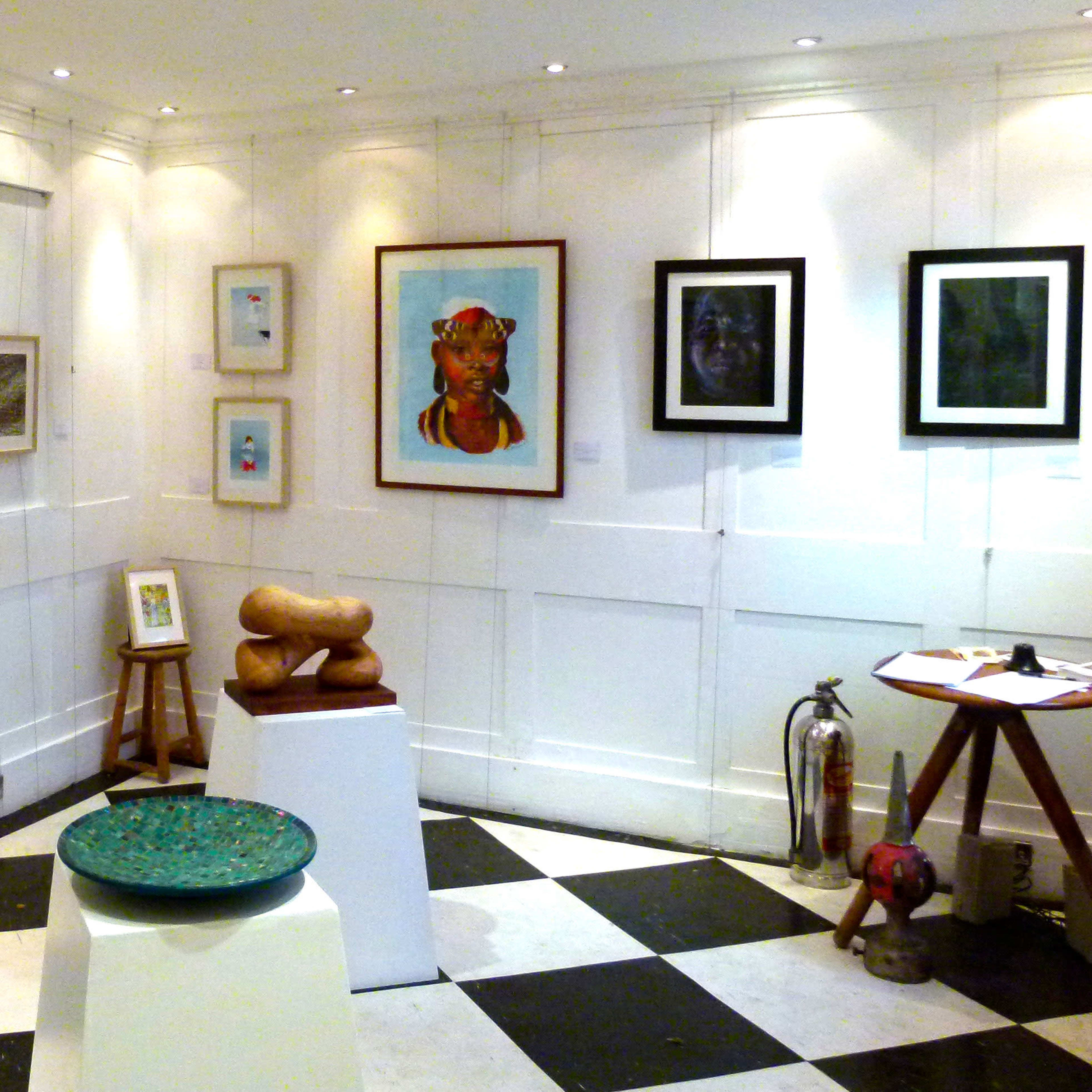 An art gallery interior with various framed artworks displayed on white walls, a globe in the corner, and a mix of sculptures and tables on a black and white checkered floor.