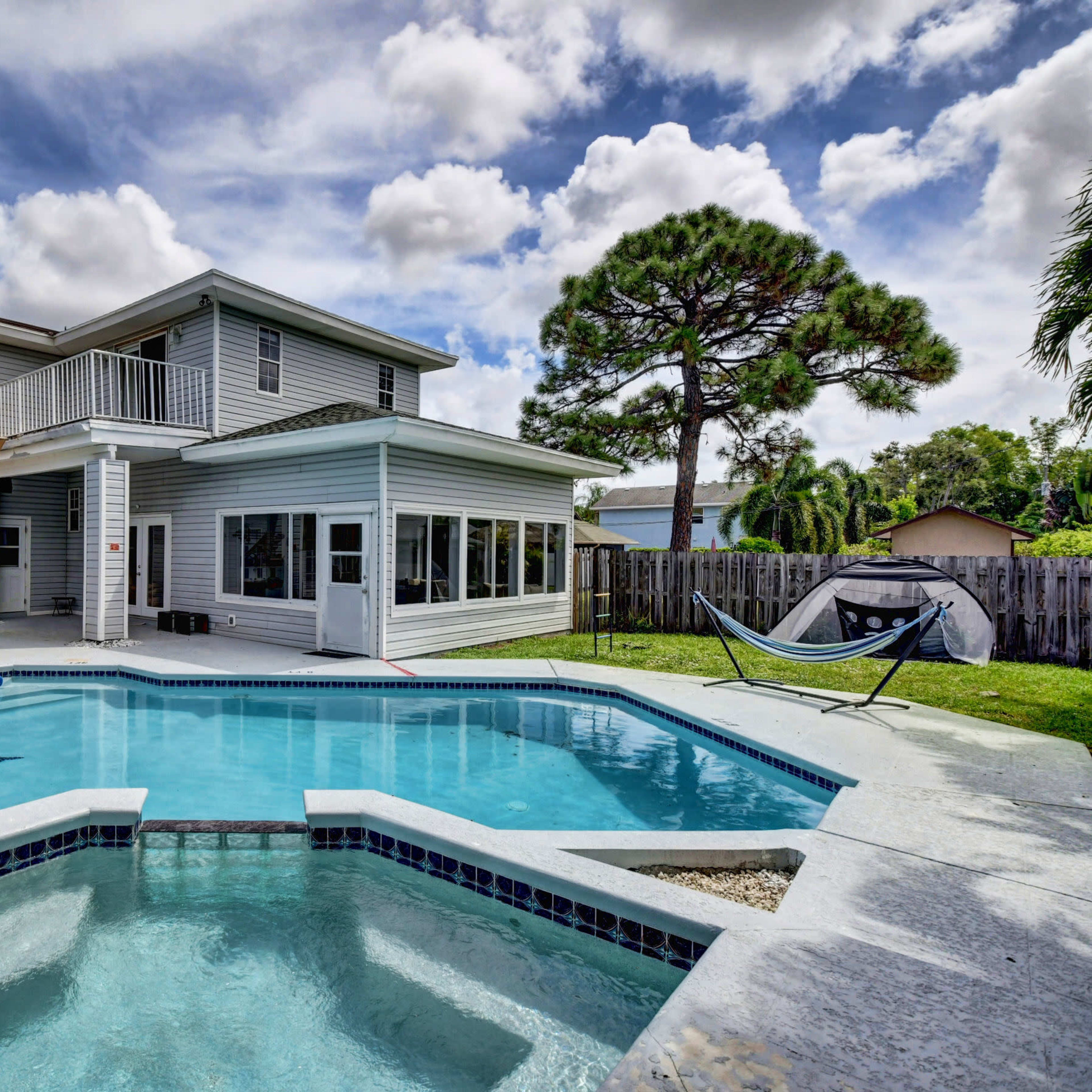 A two-story house with a swimming pool and a patio area featuring an umbrella and a hammock in the backyard.
