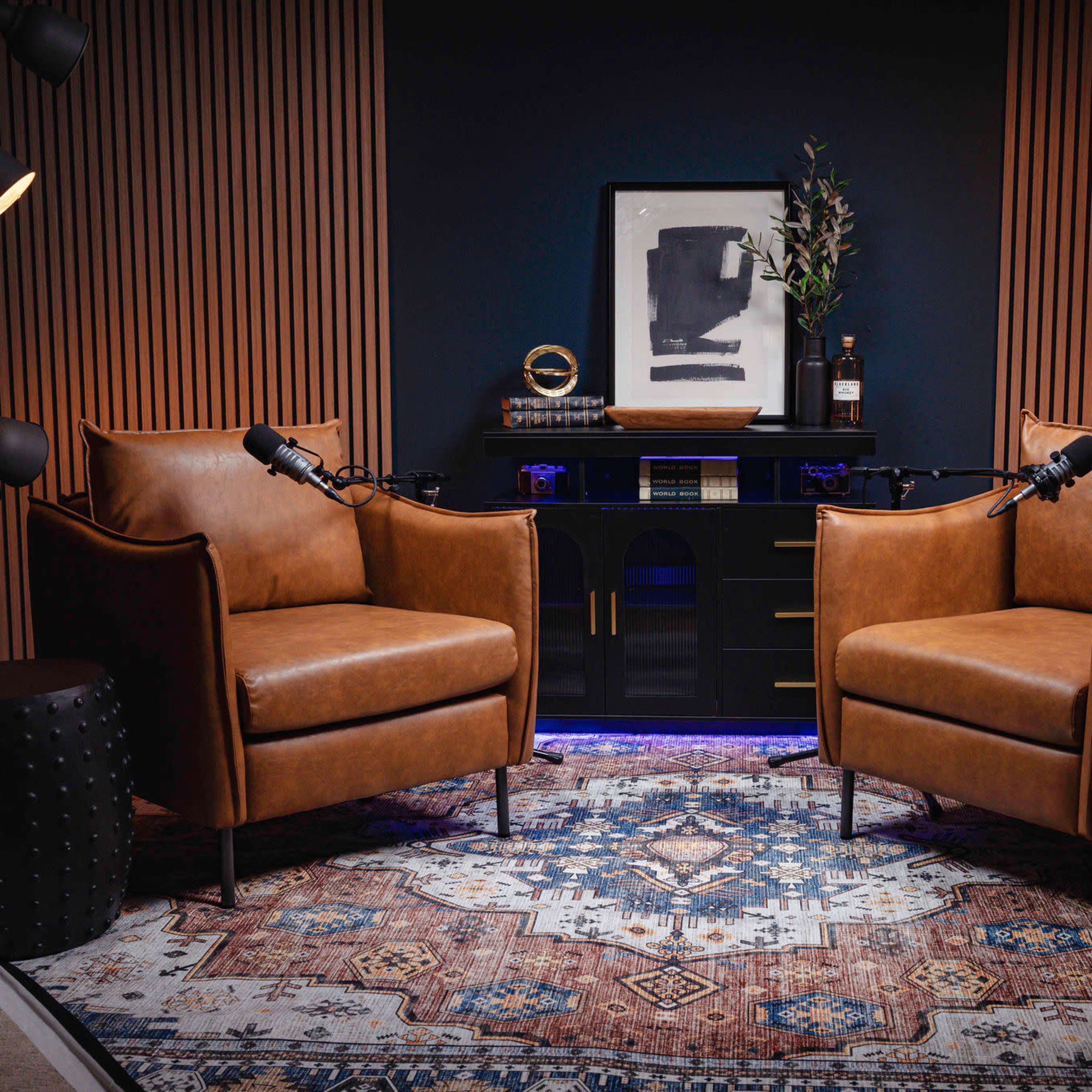 Two brown leather chairs positioned facing each other on a patterned rug, with a dark wood desk and decorative items in the background.