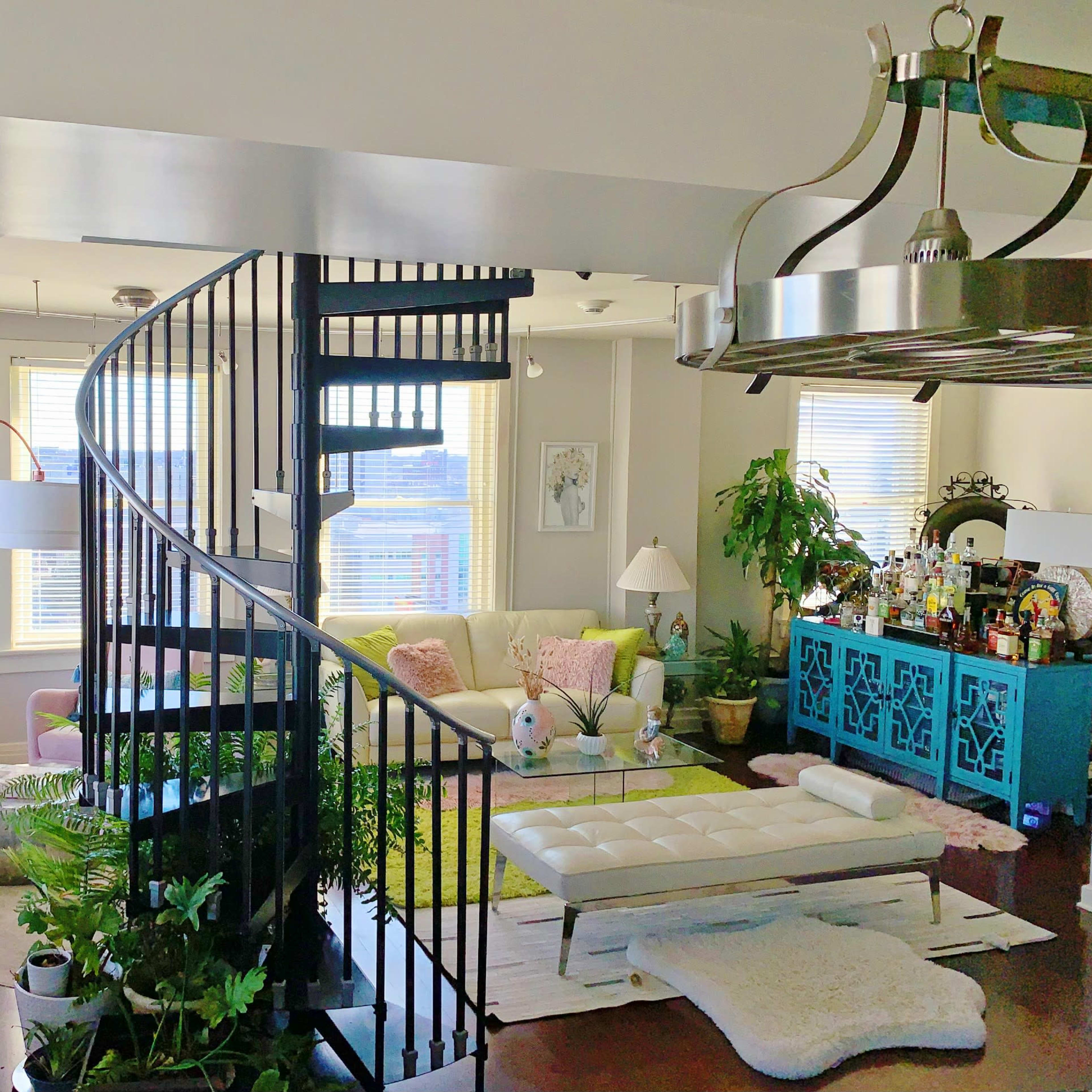 A modern living room with a spiral staircase, featuring colorful furniture, plants, and artistic decor.