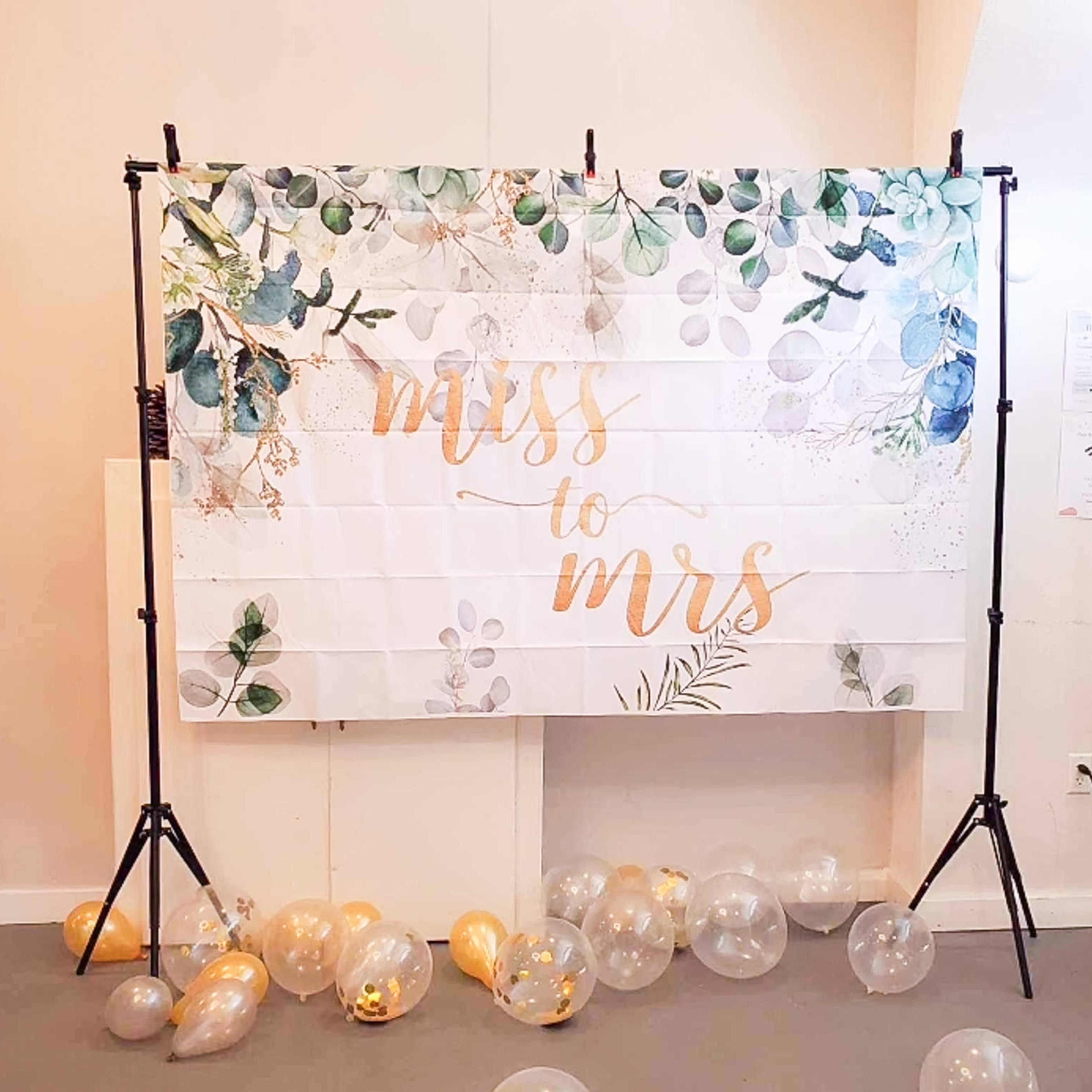 A backdrop with the phrase "Miss to Mrs" is set up on stands, surrounded by clear balloons on the floor.