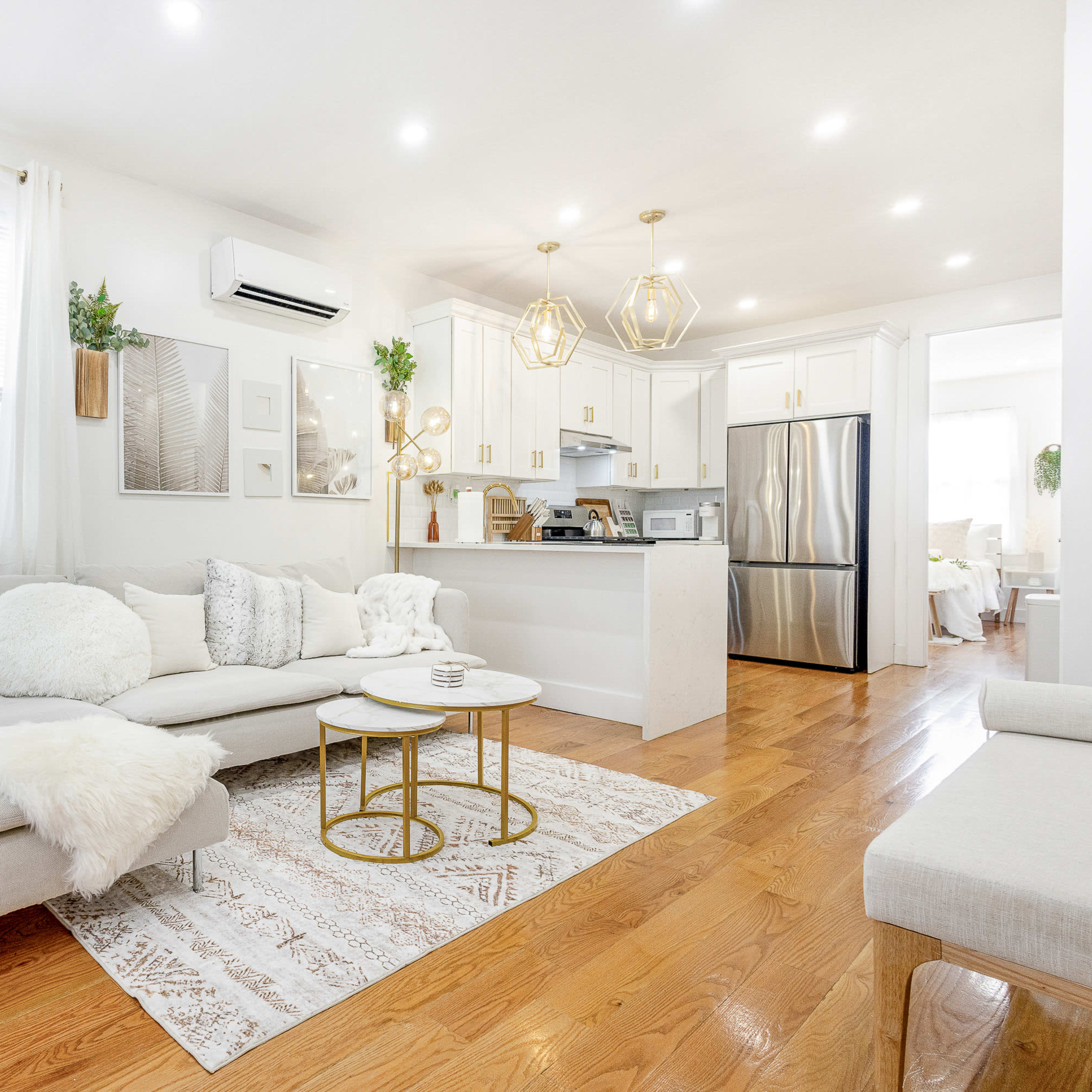 A bright and airy living room with a light-colored sectional sofa, a coffee table, and a modern kitchen in the background.