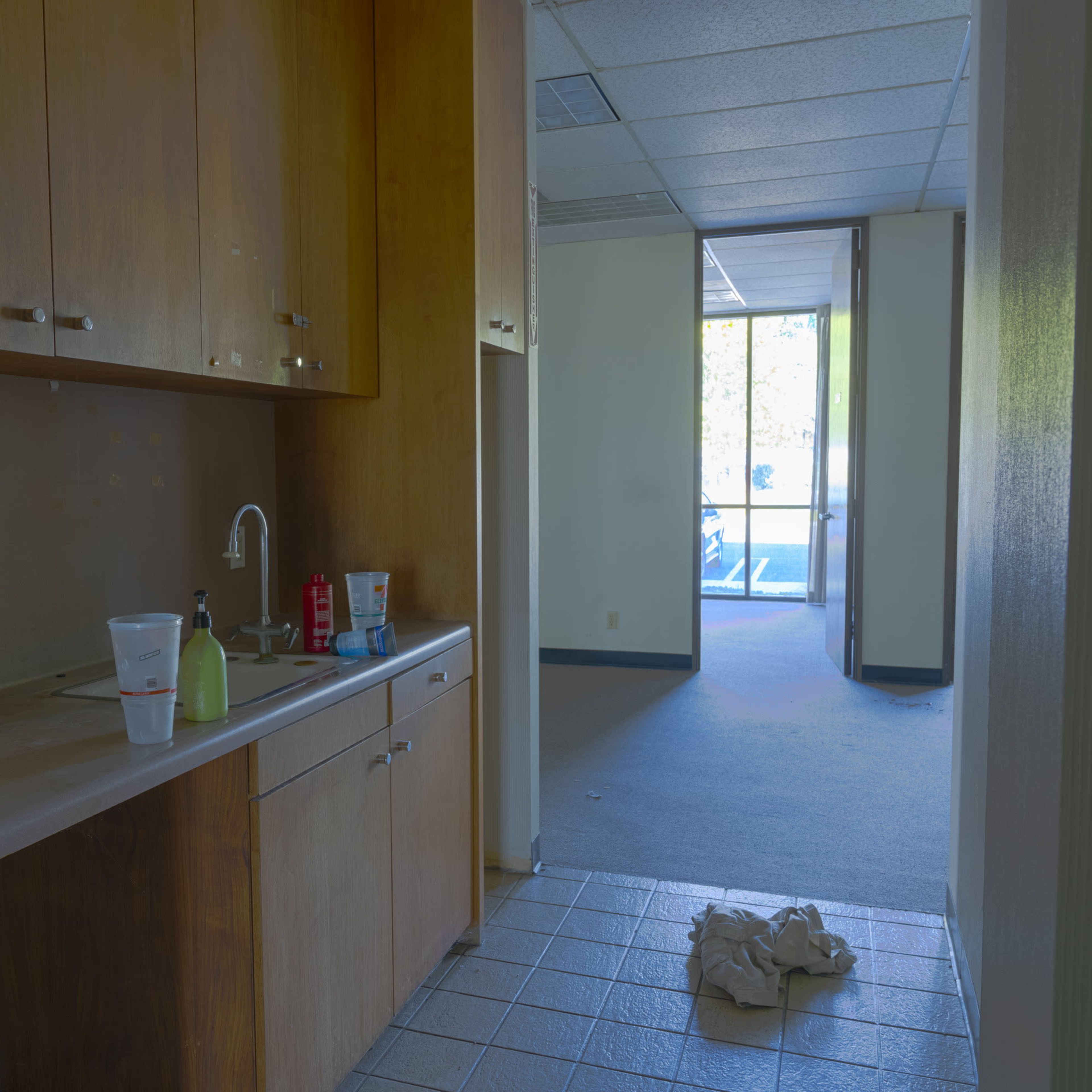 A vacant interior with a small kitchenette, an empty hallway, and large windows letting in light.