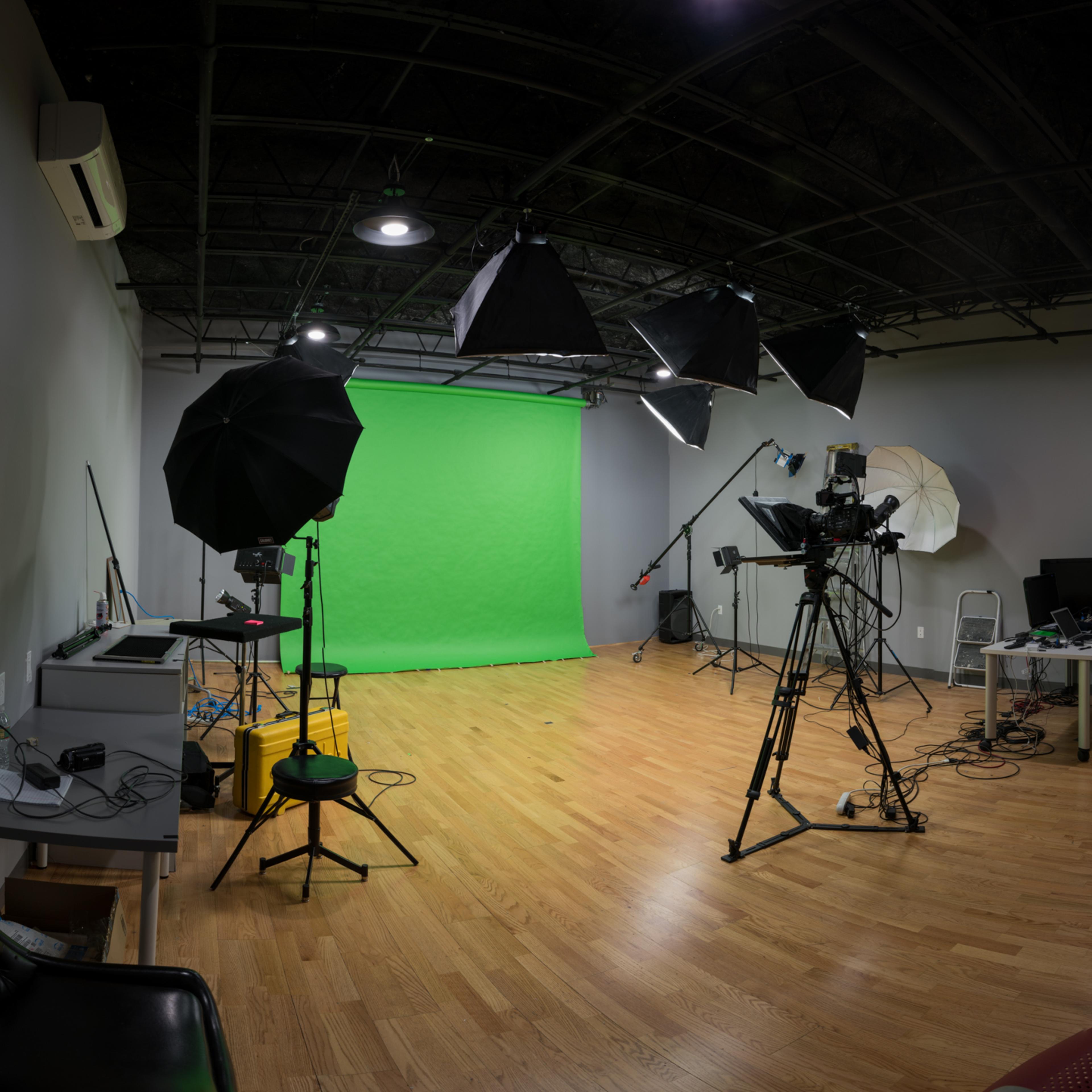 A photography studio equipped with a green screen, lighting equipment, and a camera setup on a wooden floor.