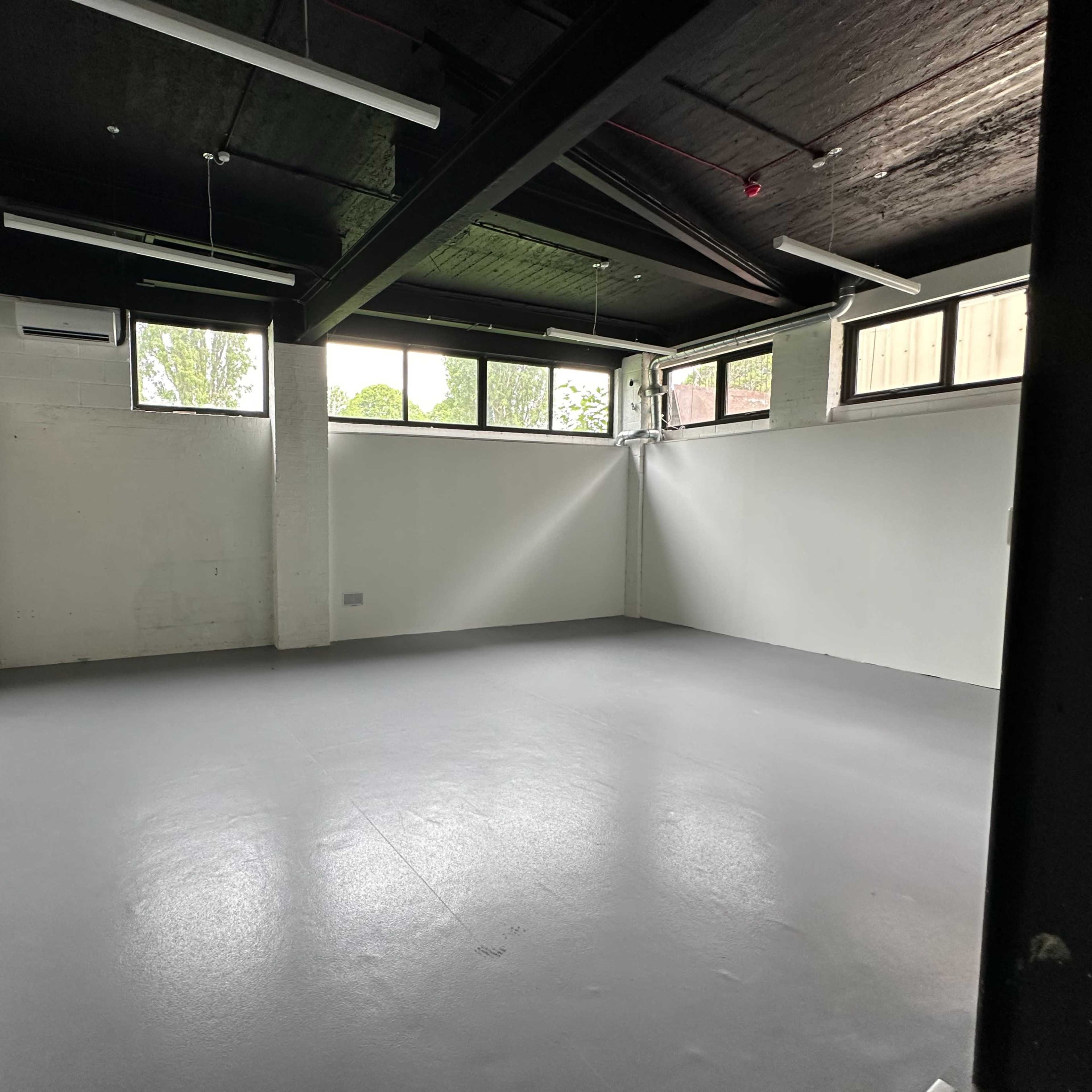 An empty room with large windows, a grey floor, and one wall featuring mirrors.