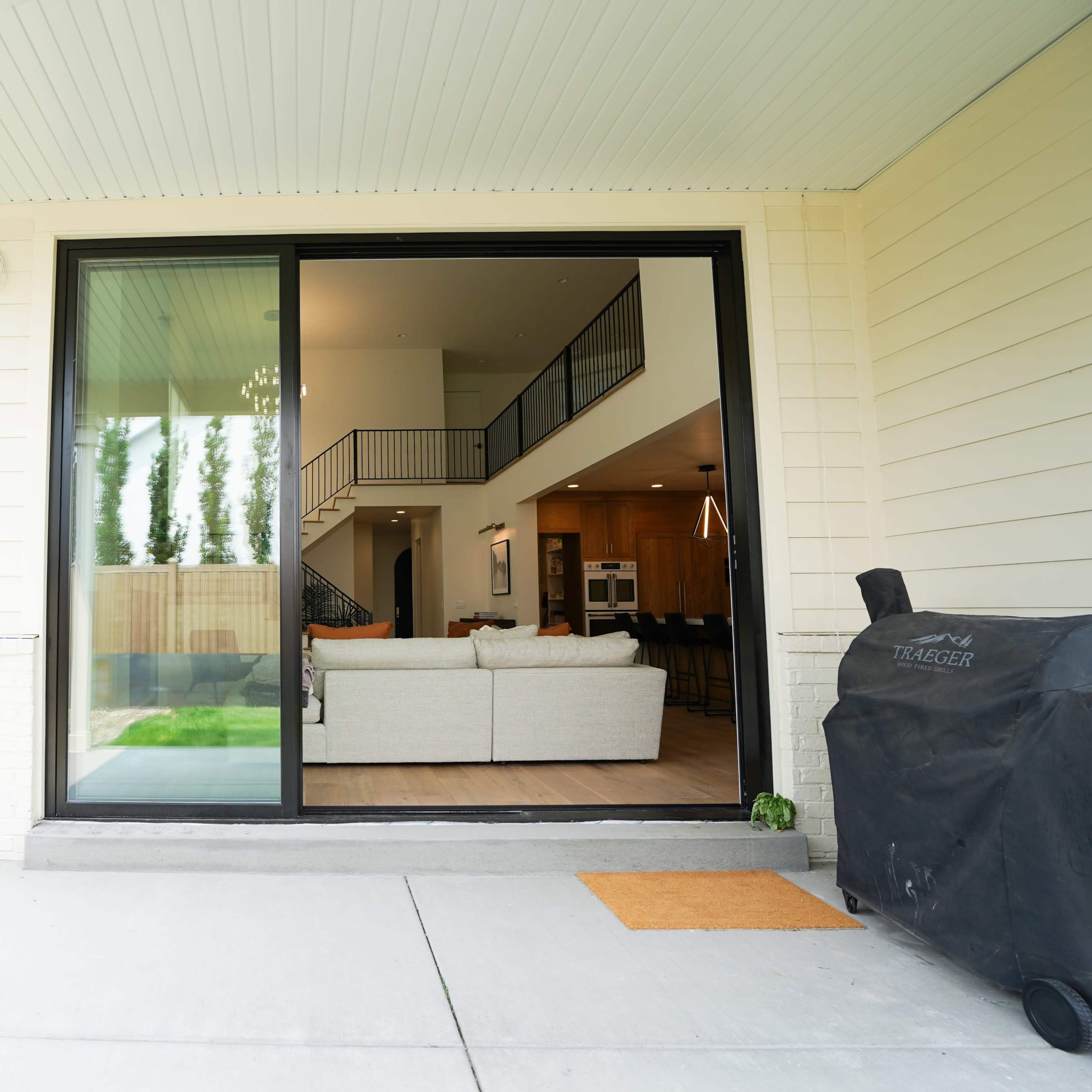 A view from a patio into a modern living space with large windows and a sofa set visible inside.