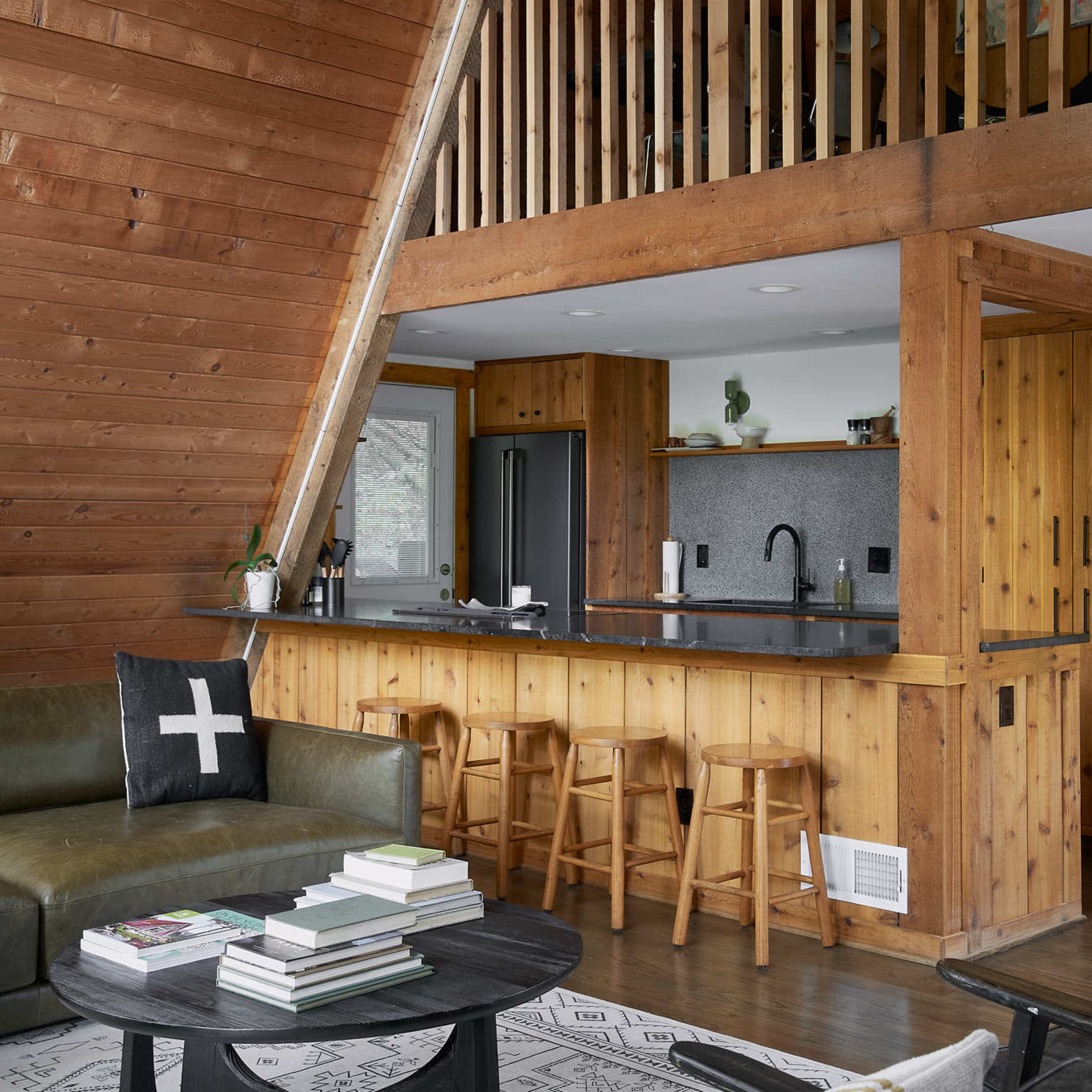 A modern cabin interior features wooden walls, a kitchen with bar seating, and a living area with a couch and coffee table.