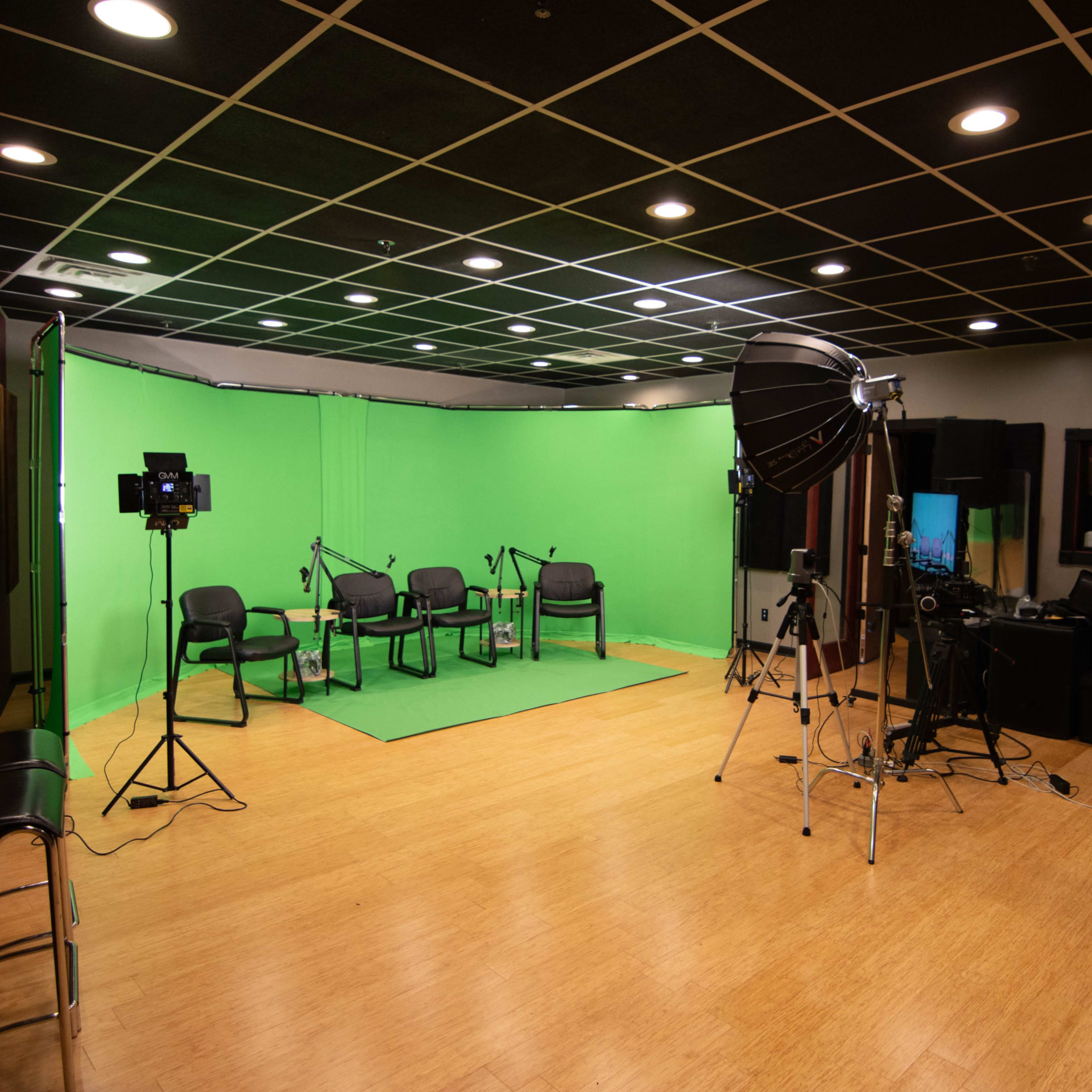 A recording studio featuring a green screen backdrop, several chairs, and various lighting equipment.