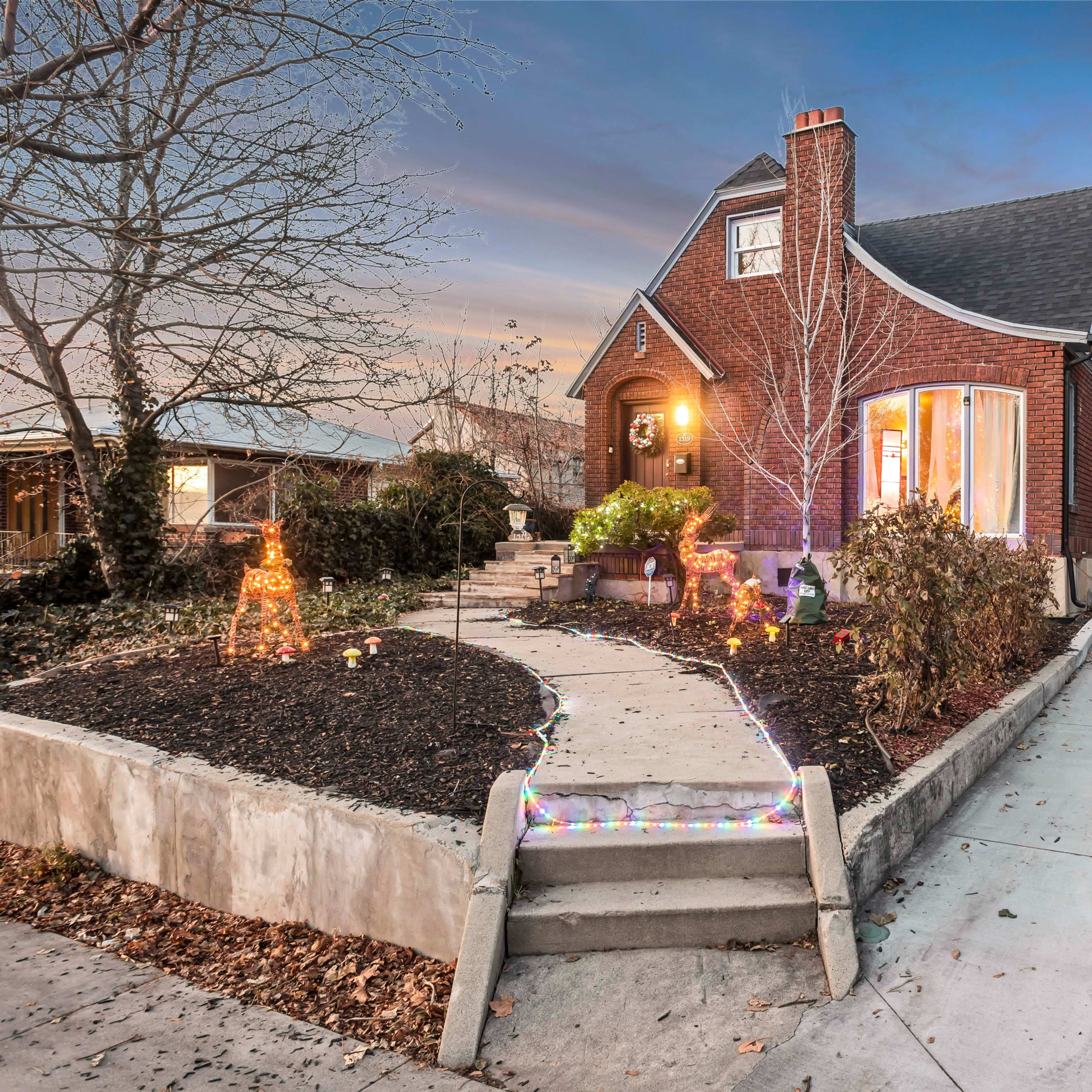 A brick house with a curved front window, surrounded by landscaped gardens and a driveway leading to a side gate.