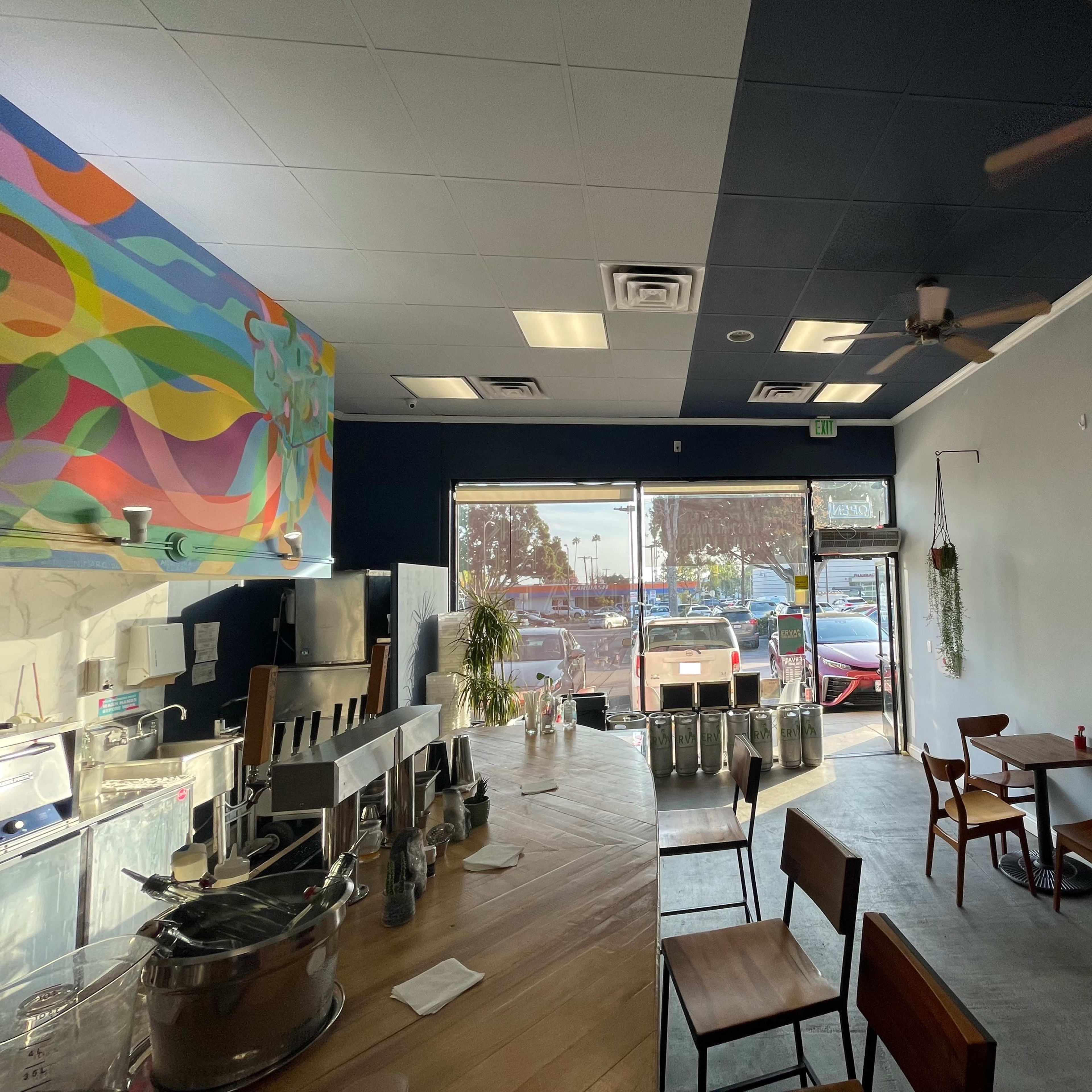 A modern café interior with a colorful mural, wooden tables, and a large window displaying outdoor scenery.