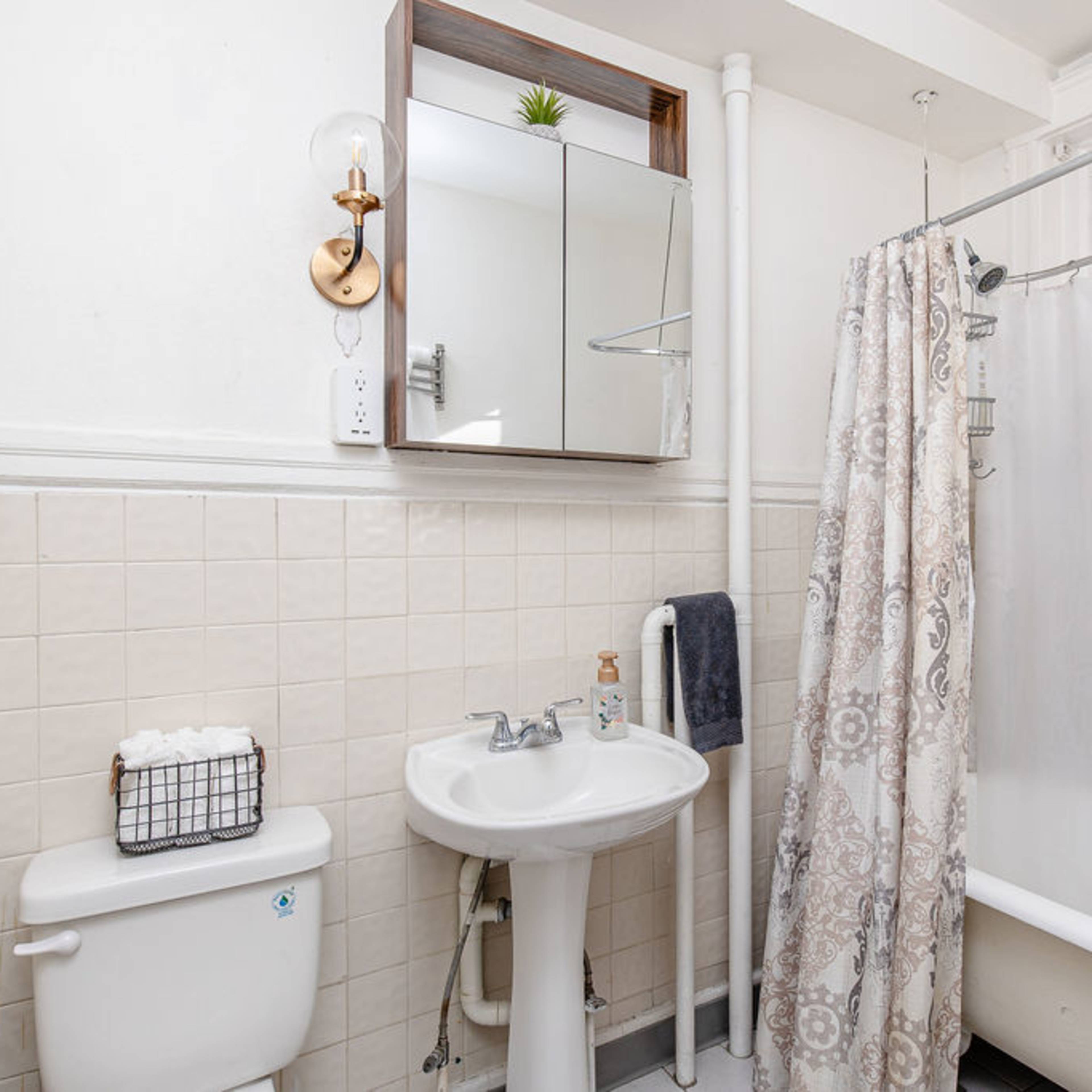 A small bathroom with a sink and a shower curtain over a bathtub, featuring tiled walls and a mirror mounted above the sink.