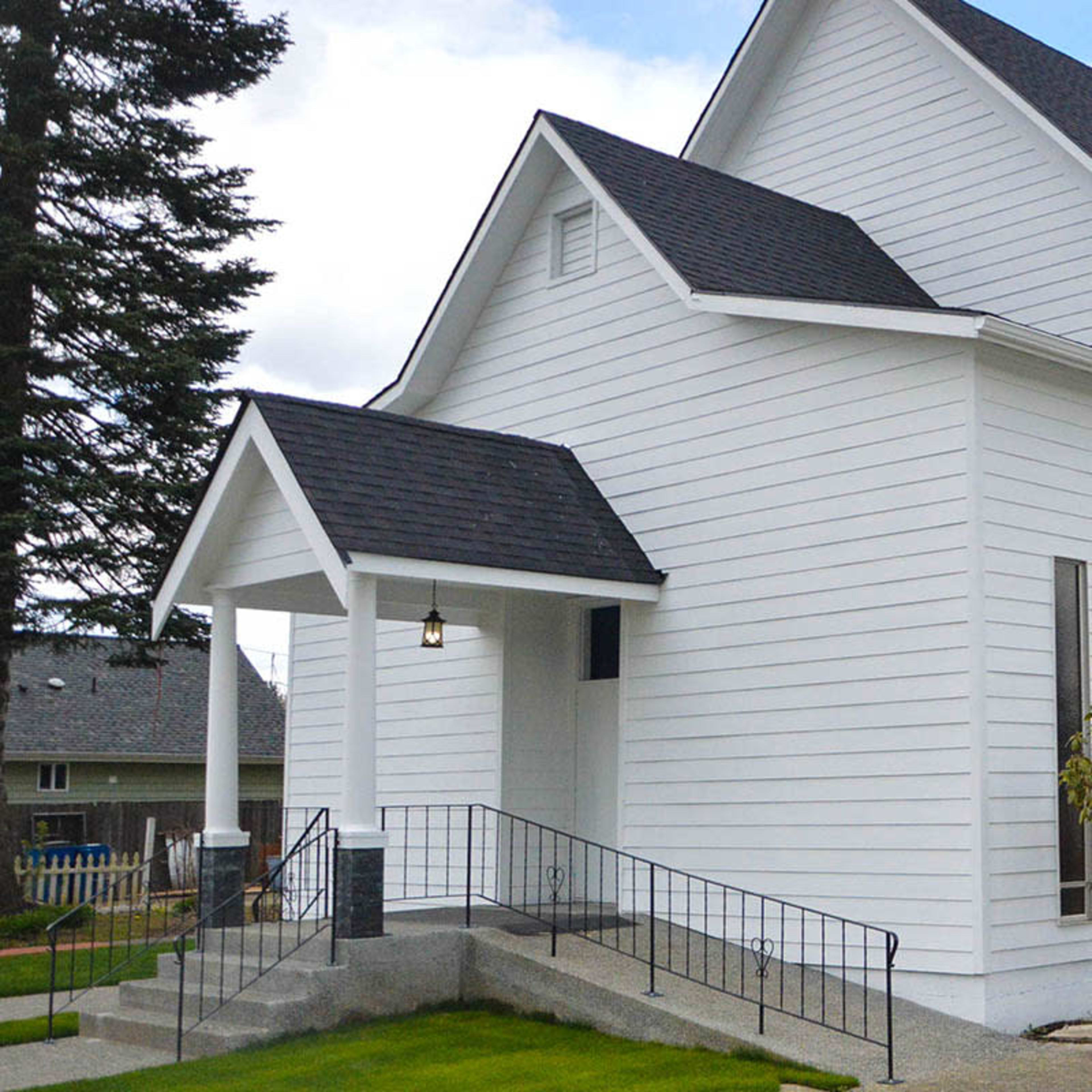 A white church building with a gabled roof, a small entrance porch, and a well-maintained ramp leading to the entrance.