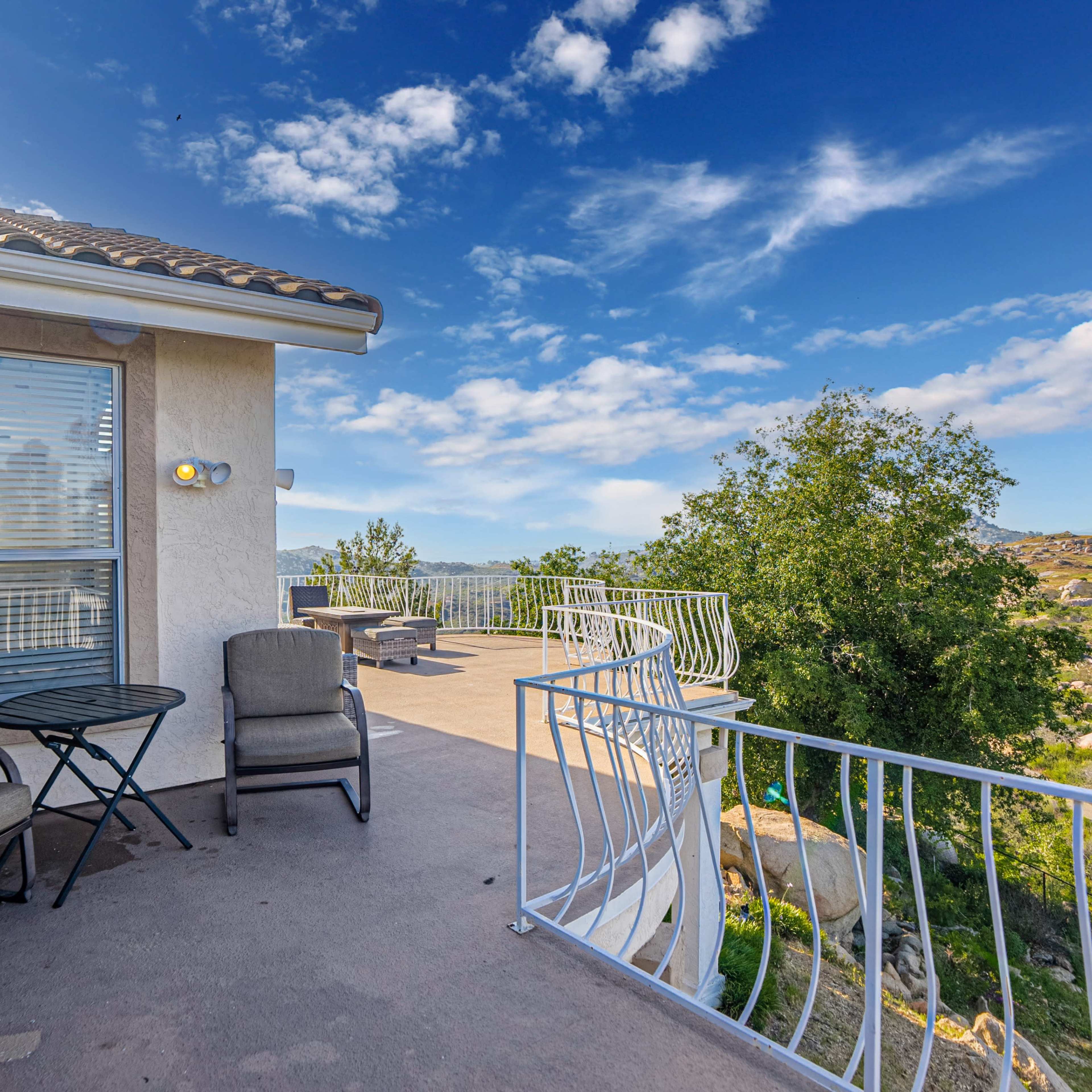 A patio features two chairs and a small table, overlooking a scenic landscape with rolling hills and a blue sky.