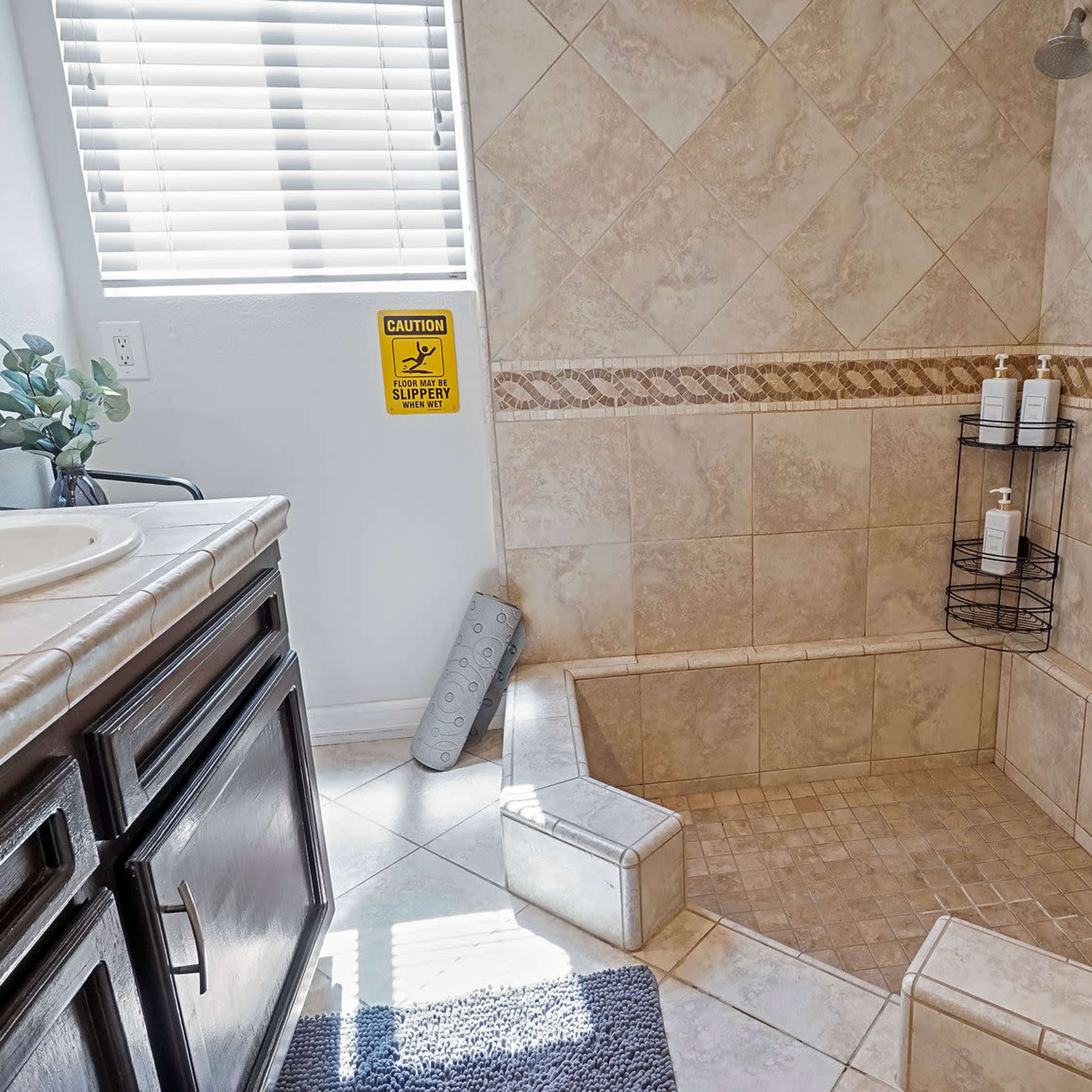 A tiled shower area with a built-in bench, a wall-mounted showerhead, and a corner shelving unit holding toiletries.