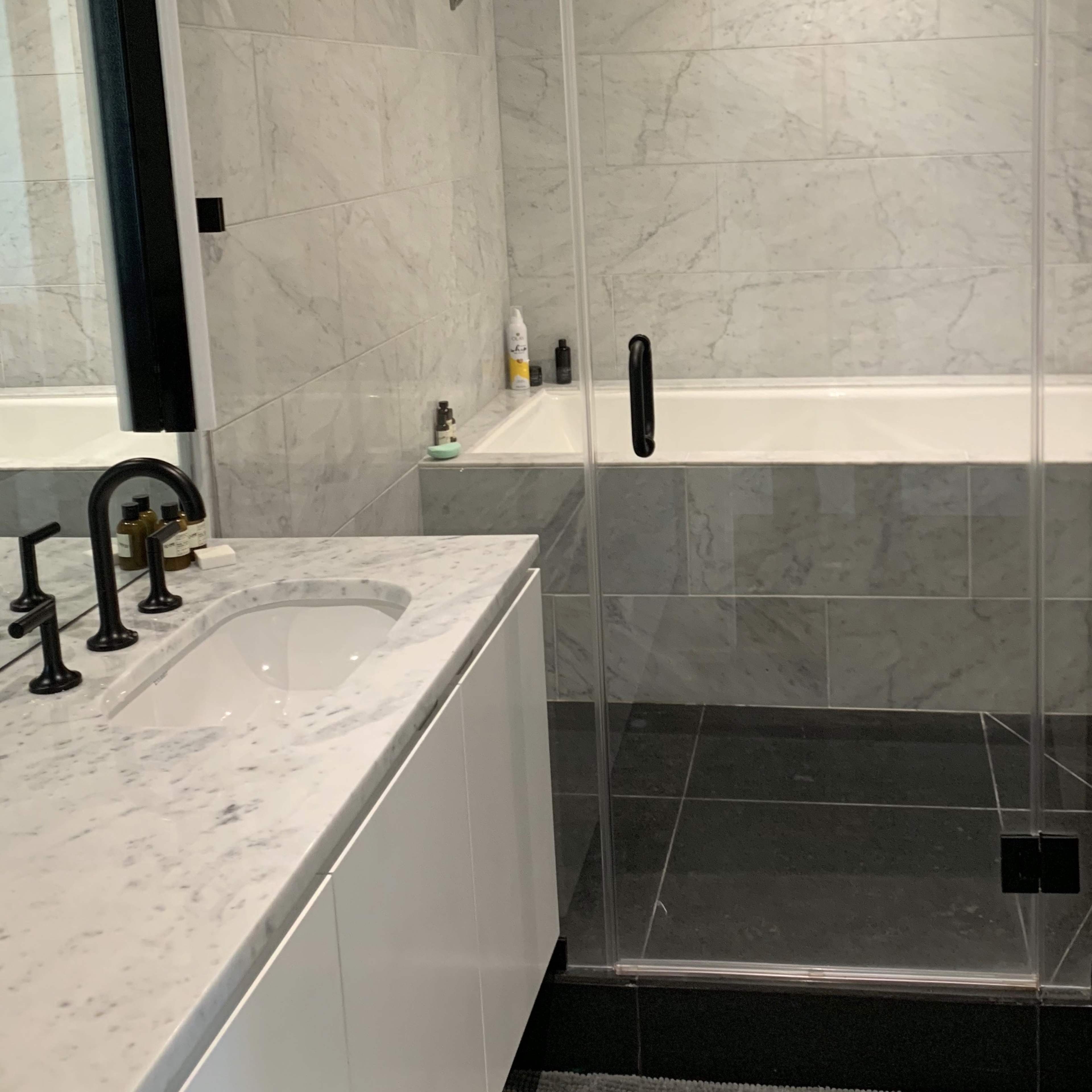 A modern bathroom featuring a glass shower enclosure, a freestanding bathtub, and a double vanity with a marble countertop.