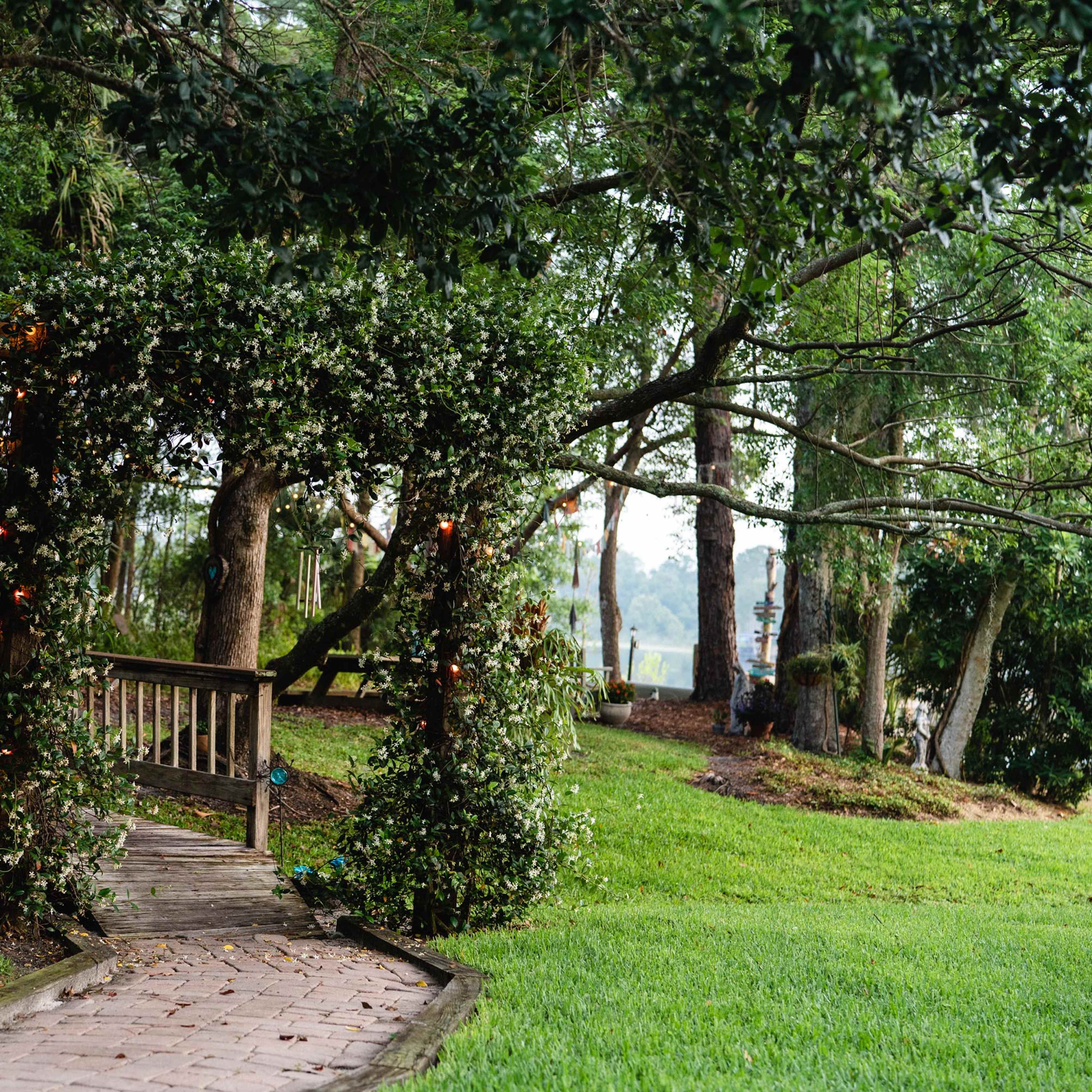 A wooden pathway leads to a covered archway adorned with greenery in a garden setting.
