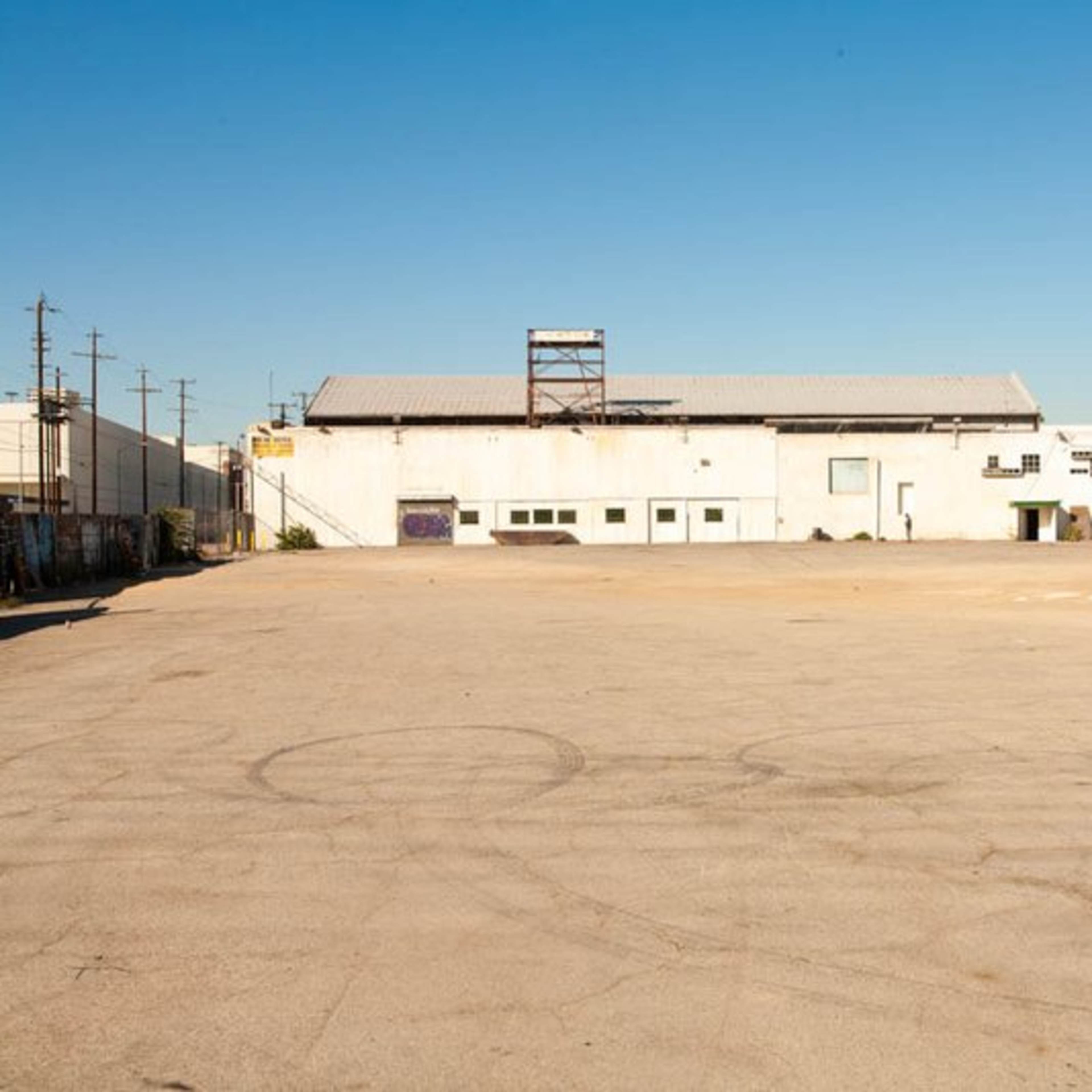 A large, empty lot with a concrete surface and a single building covered in graffiti along its perimeter.