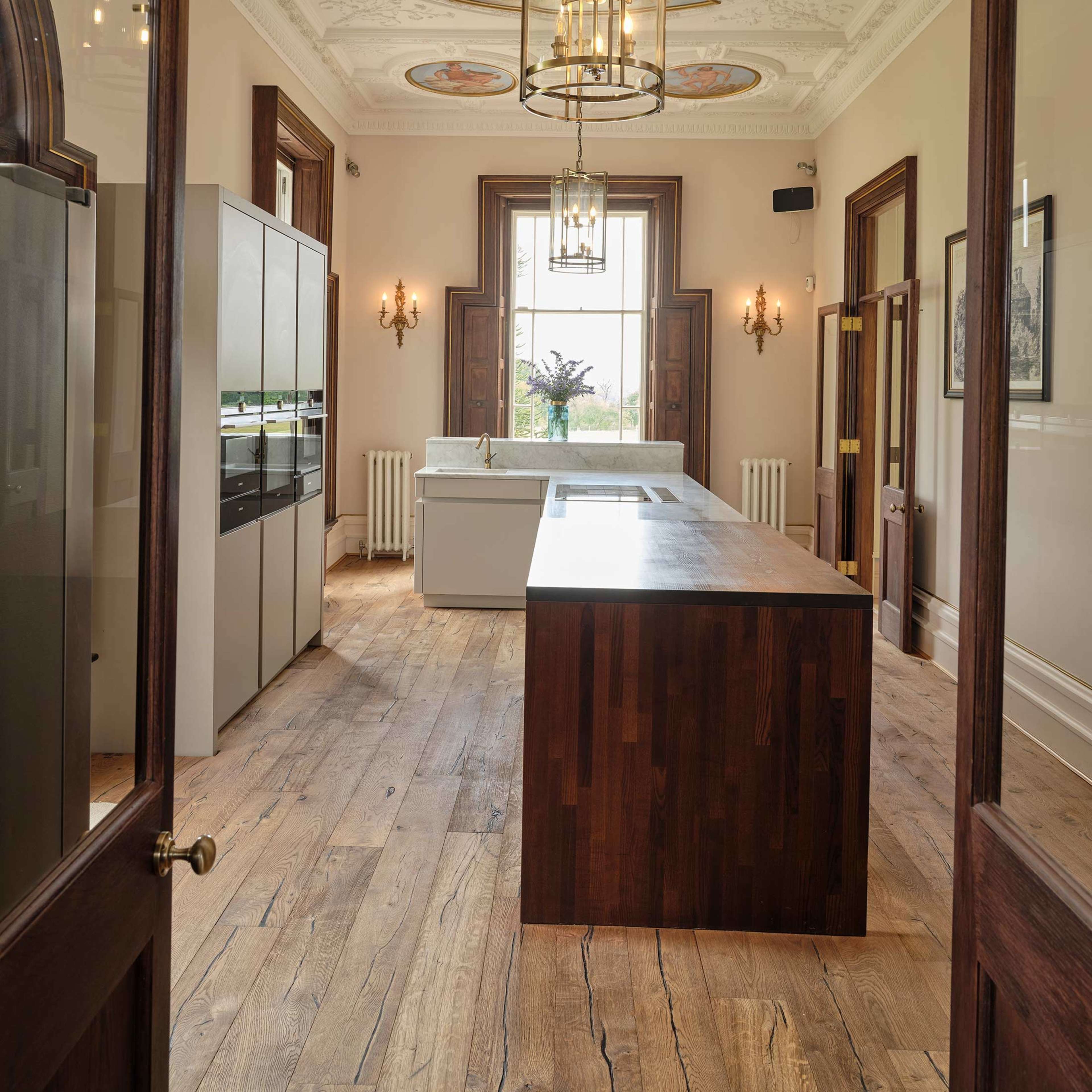 A spacious kitchen with a wooden island, decorative ceiling, and large windows allowing natural light.