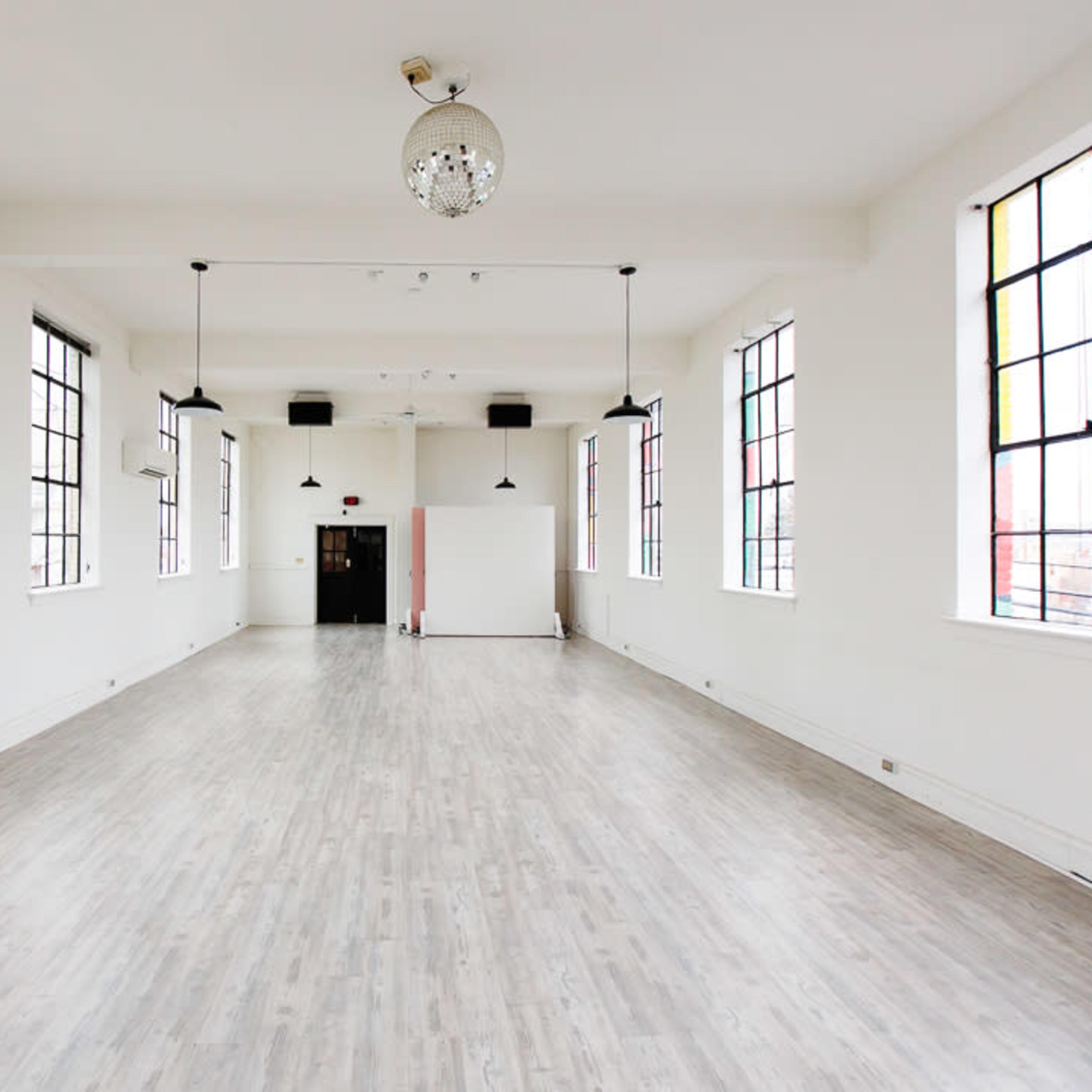A spacious, empty room with large windows, wooden flooring, and a chandelier.