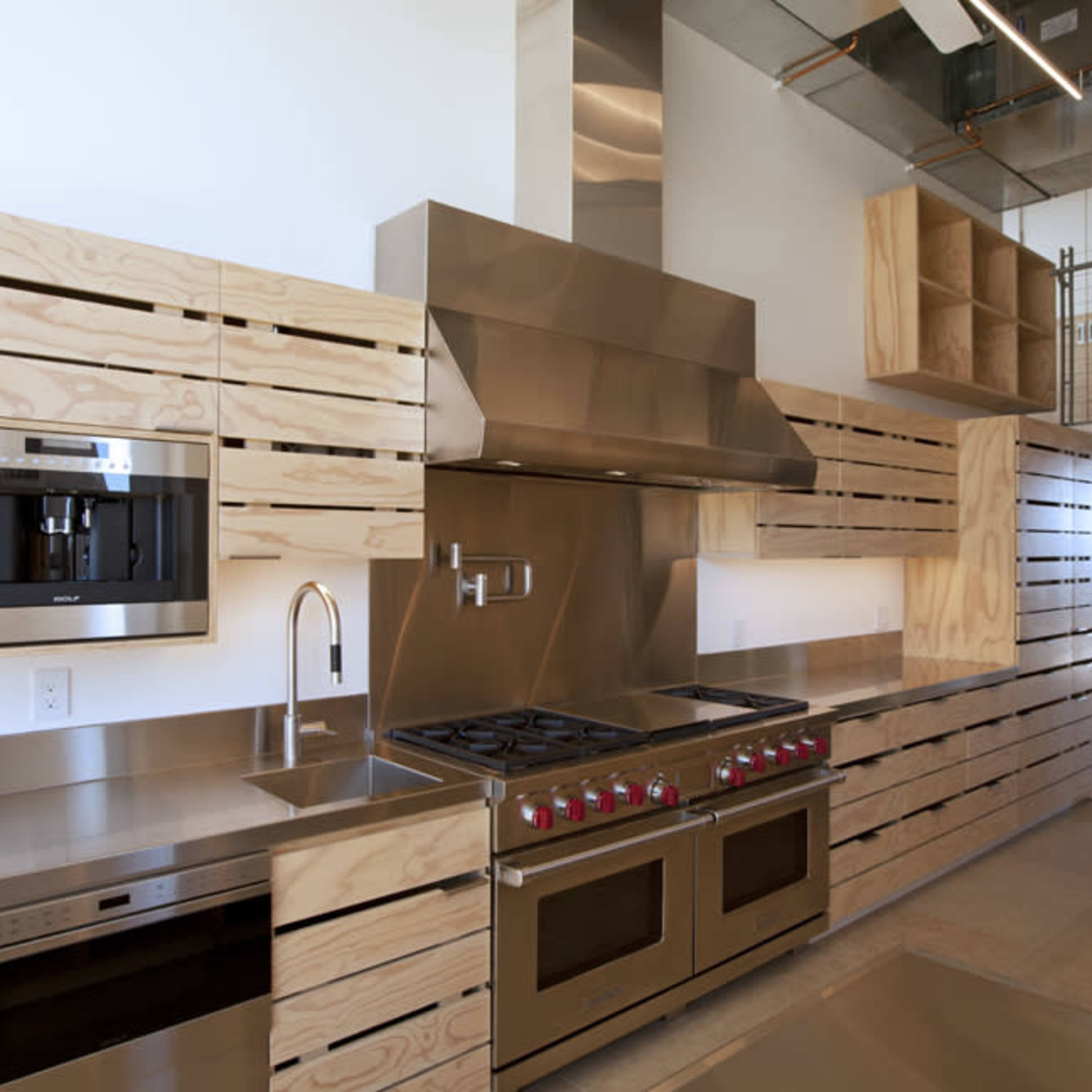 A modern kitchen with stainless steel appliances, including a gas range and built-in coffee machine, paired with plywood cabinetry and an open layout.