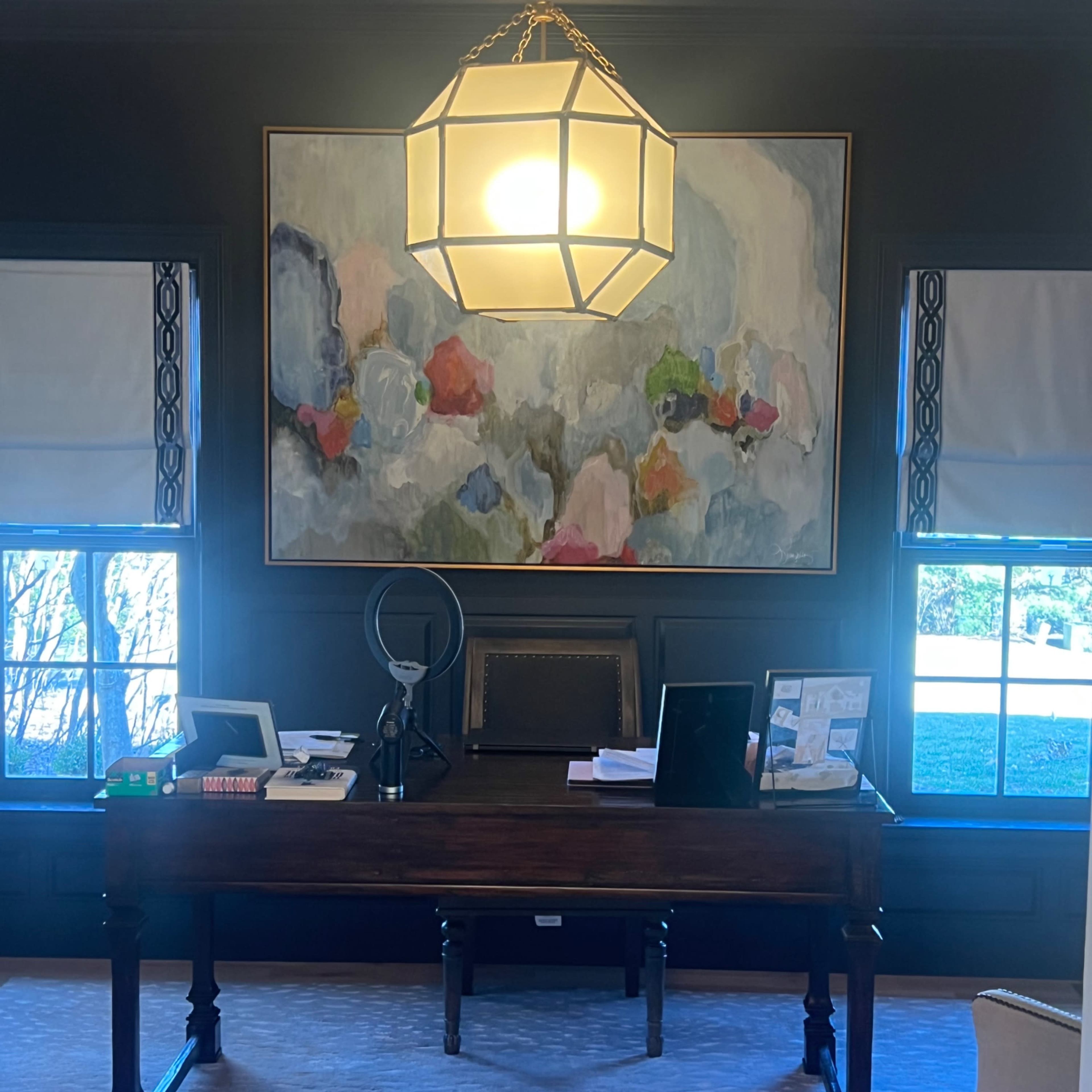 A modern office space featuring a wooden desk, a large abstract painting on the wall, and natural light coming through the windows.