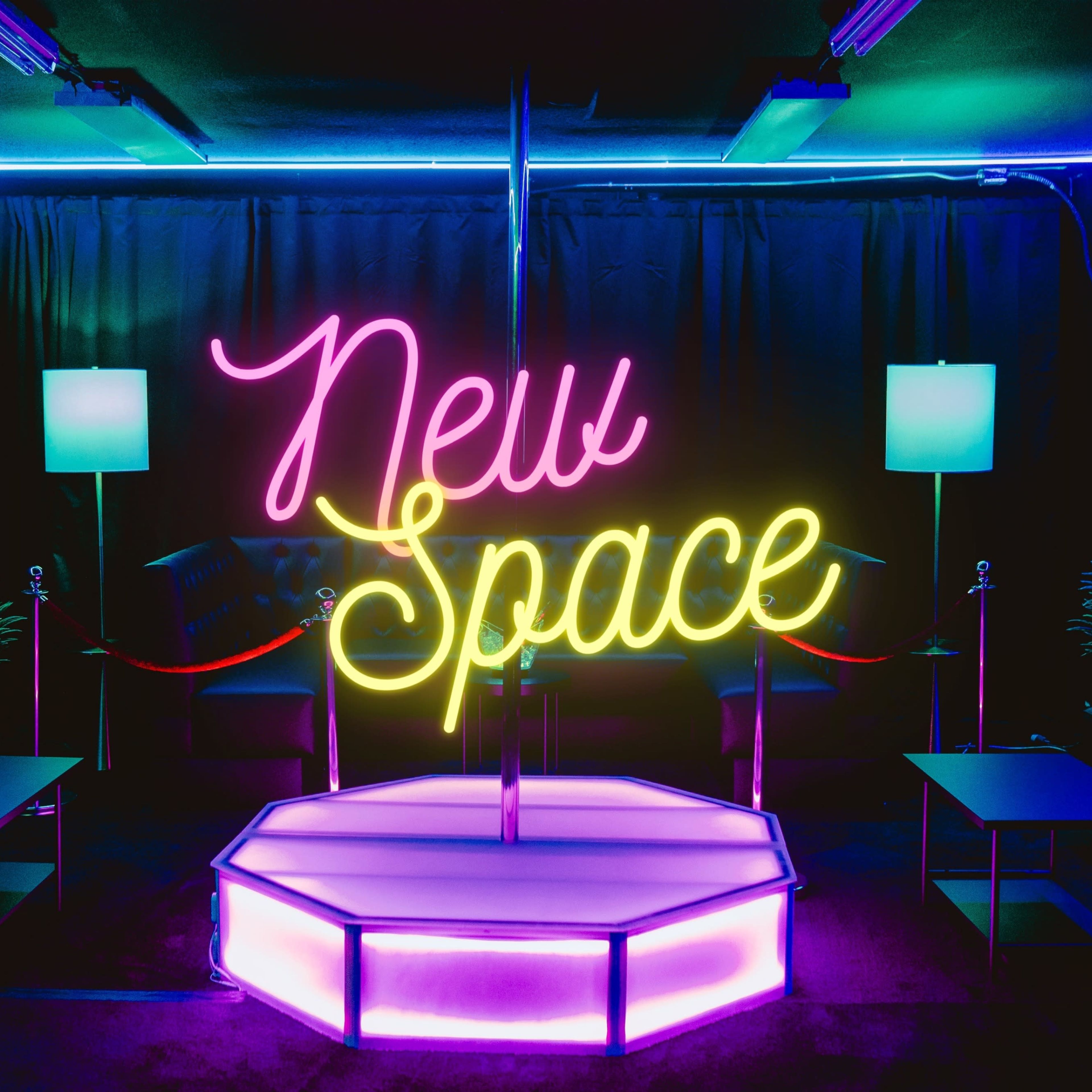 A vibrant, neon sign reading "New Space" in a dimly lit lounge area with a small stage, seating, and decorative plants.