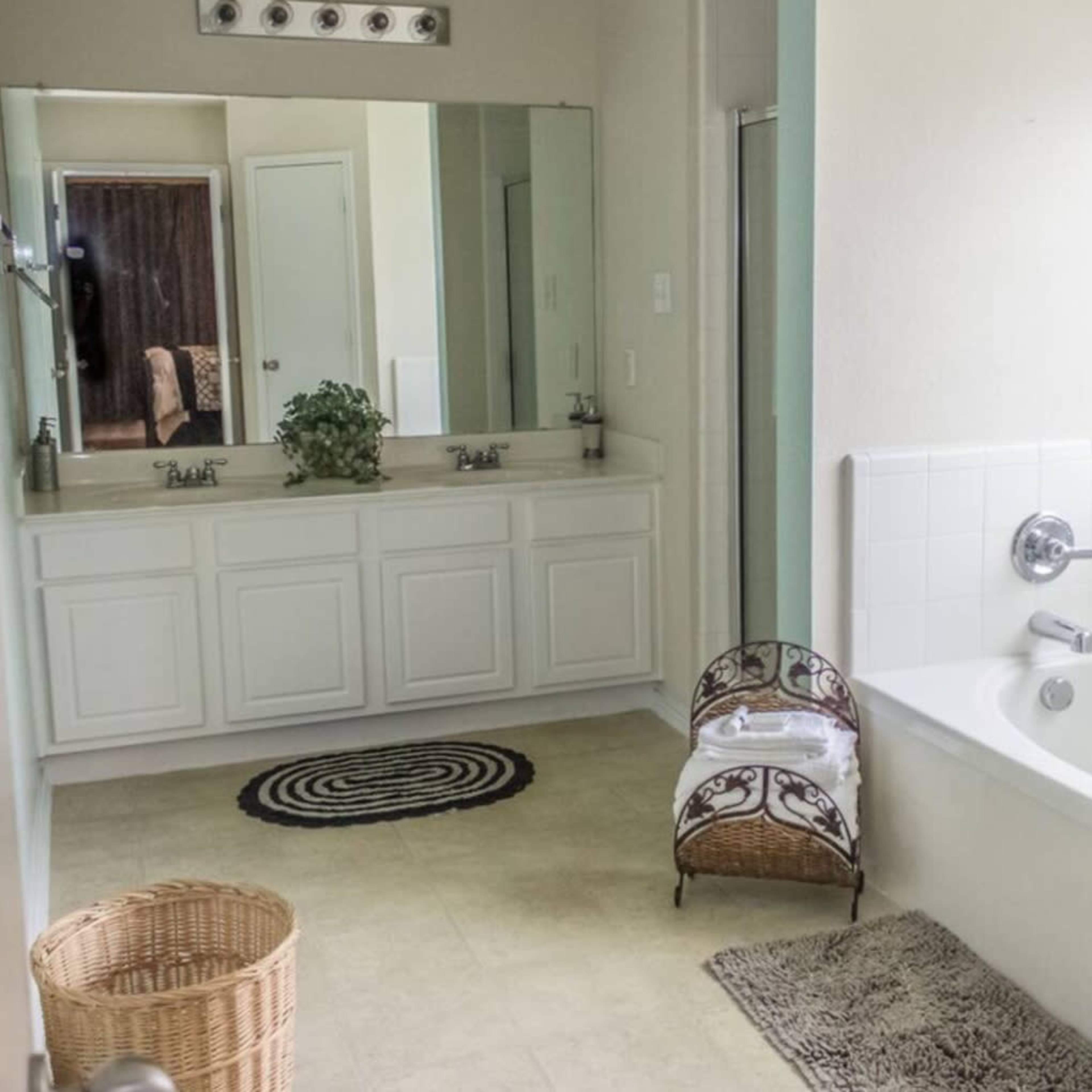 A bathroom features a double vanity with mirrors, a bathtub, and a woven basket on the floor.
