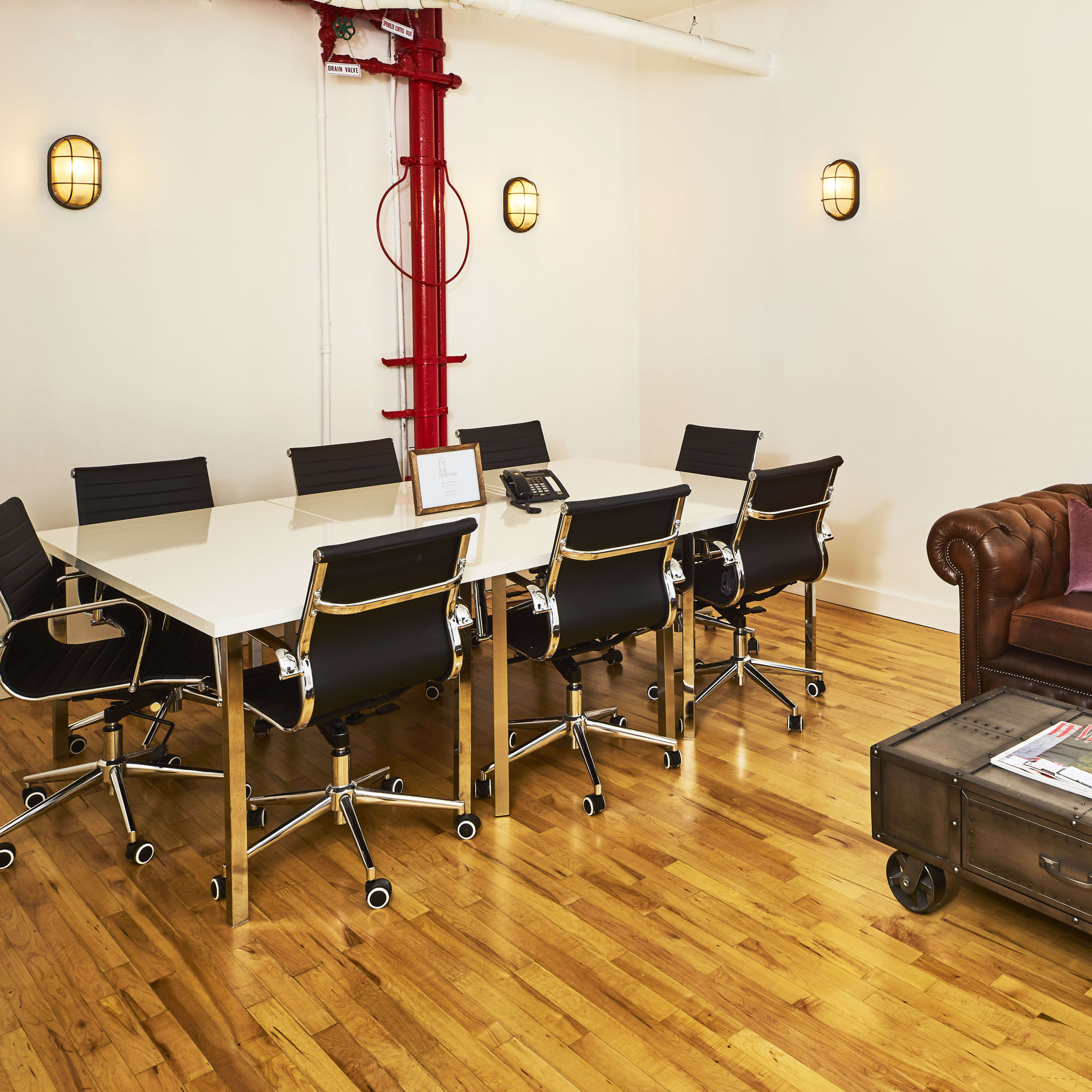 A conference room with a large white table surrounded by black chairs, a brown leather couch, and a coffee table on a hardwood floor.