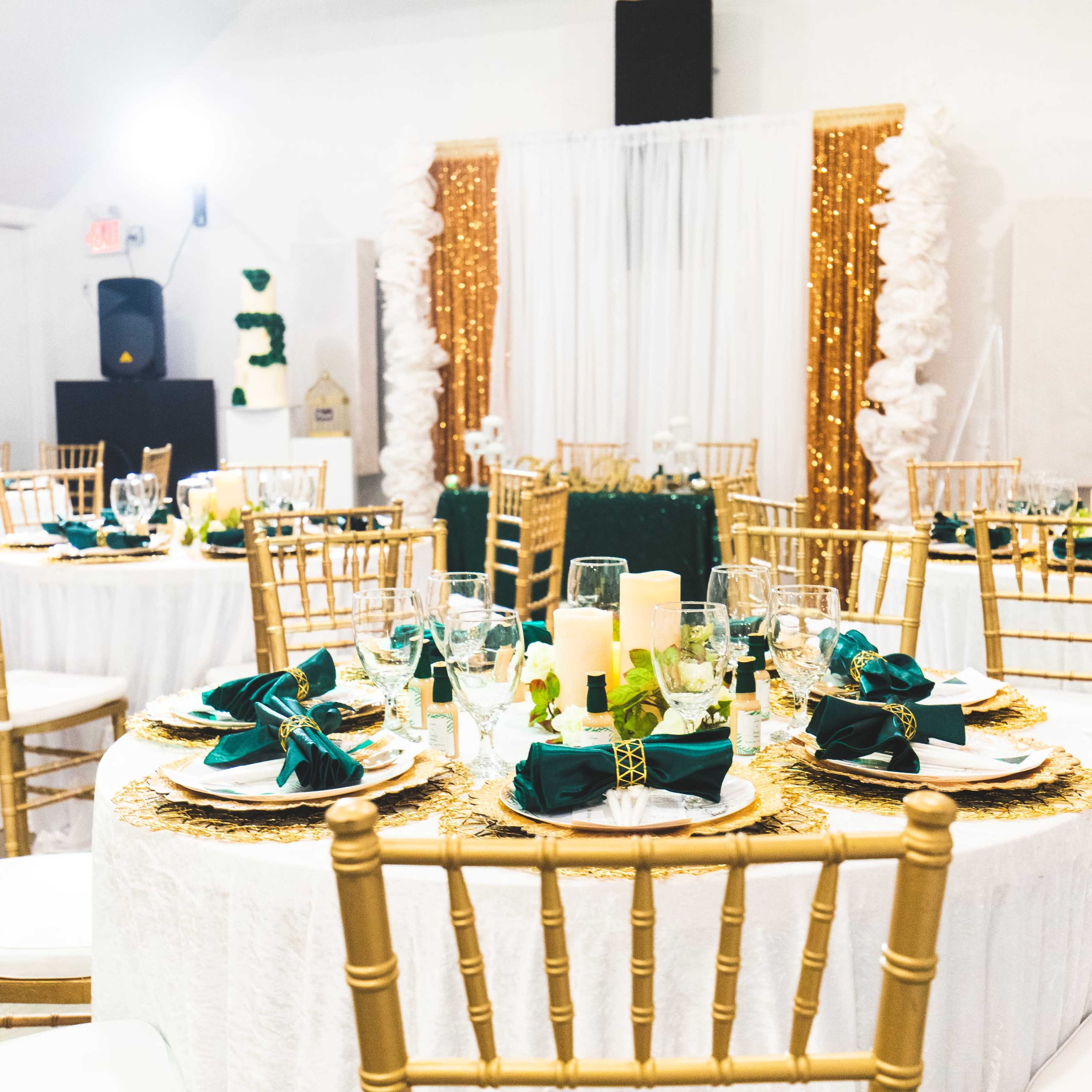 Elegantly arranged round tables with gold chairs, adorned with teal napkins and centerpieces featuring candles, in a decorated event space.