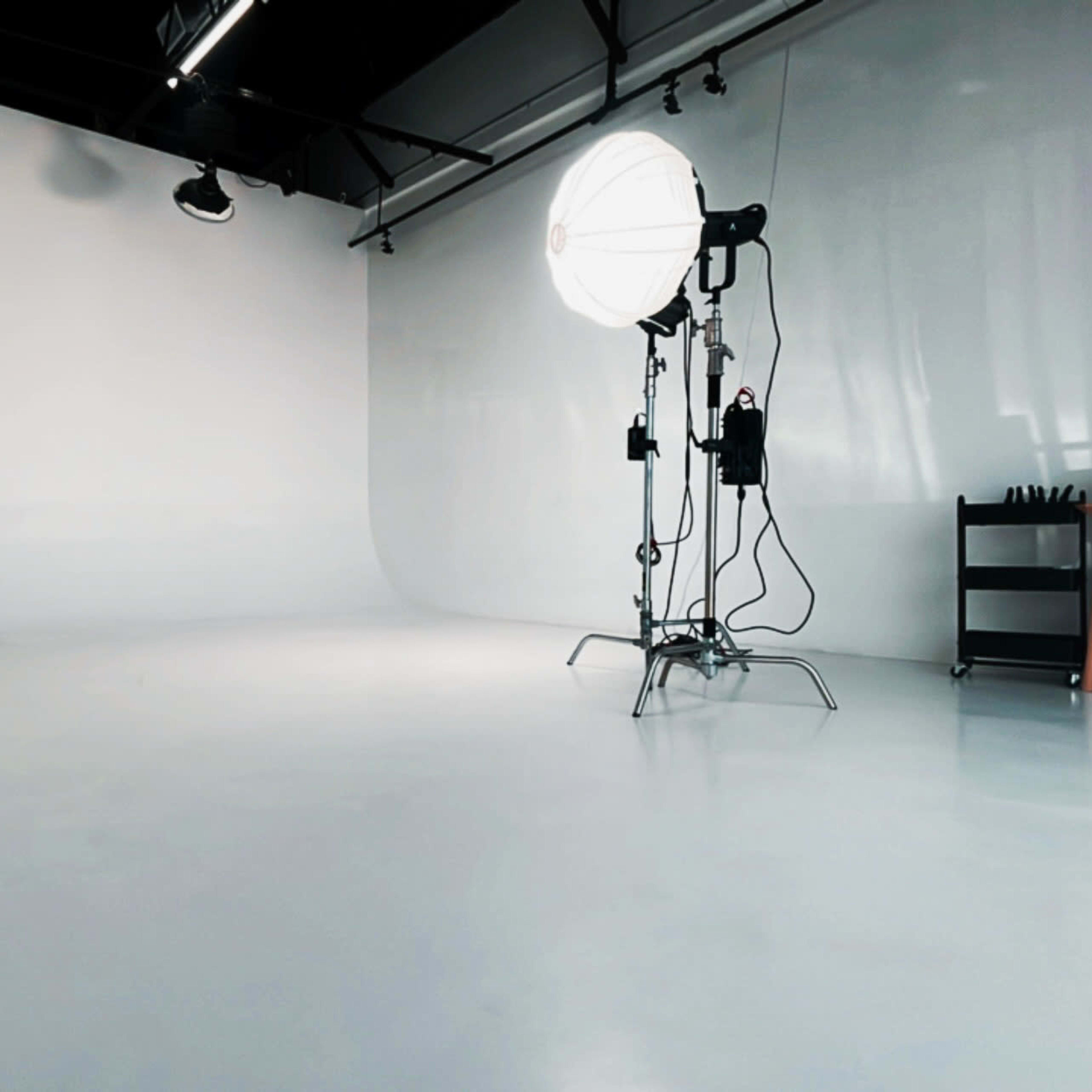 A well-lit photography studio featuring a large softbox light, a seamless backdrop, and a minimalistic setup.