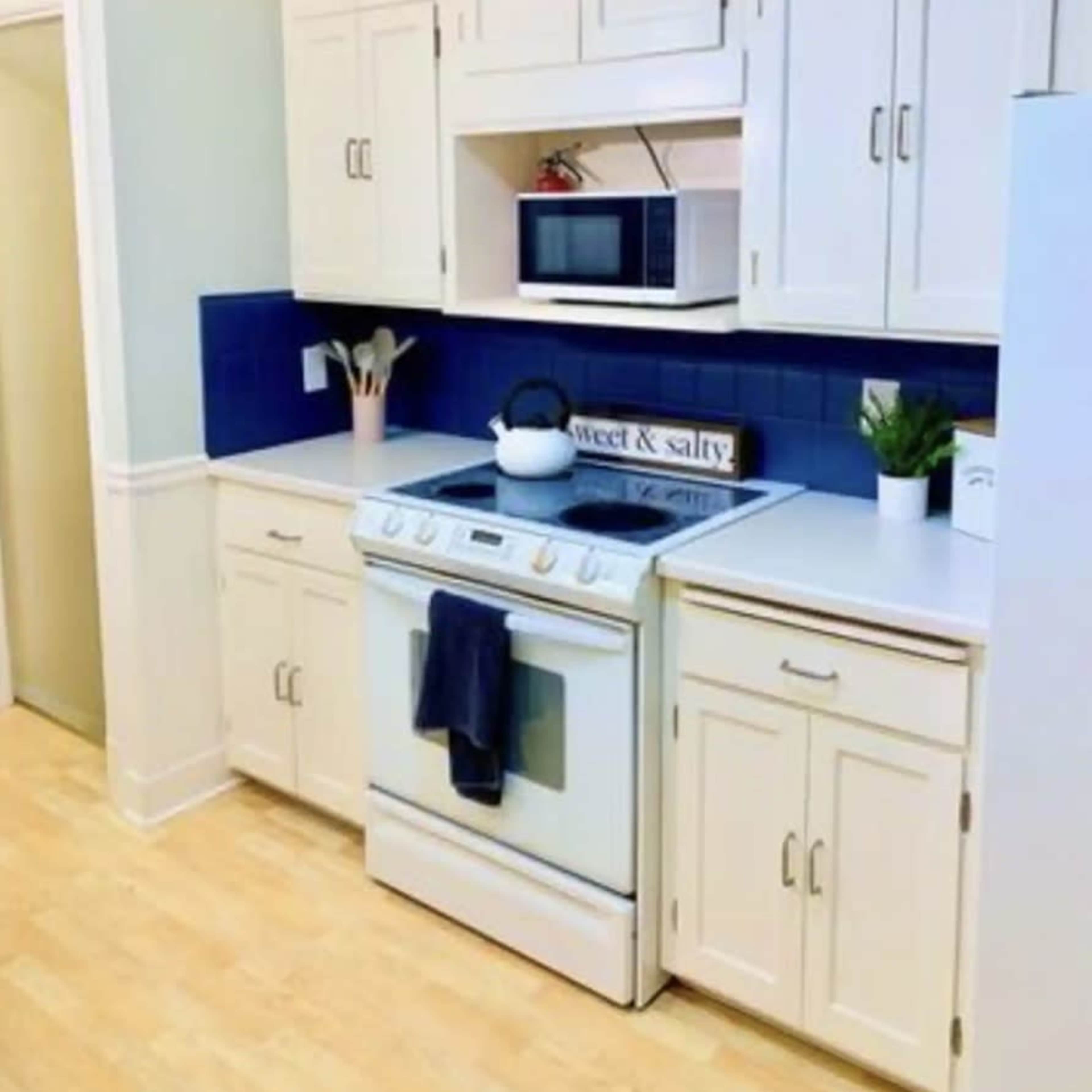 A modern kitchen with white cabinetry, a blue backsplash, a microwave above an oven, and a small plant on the countertop.