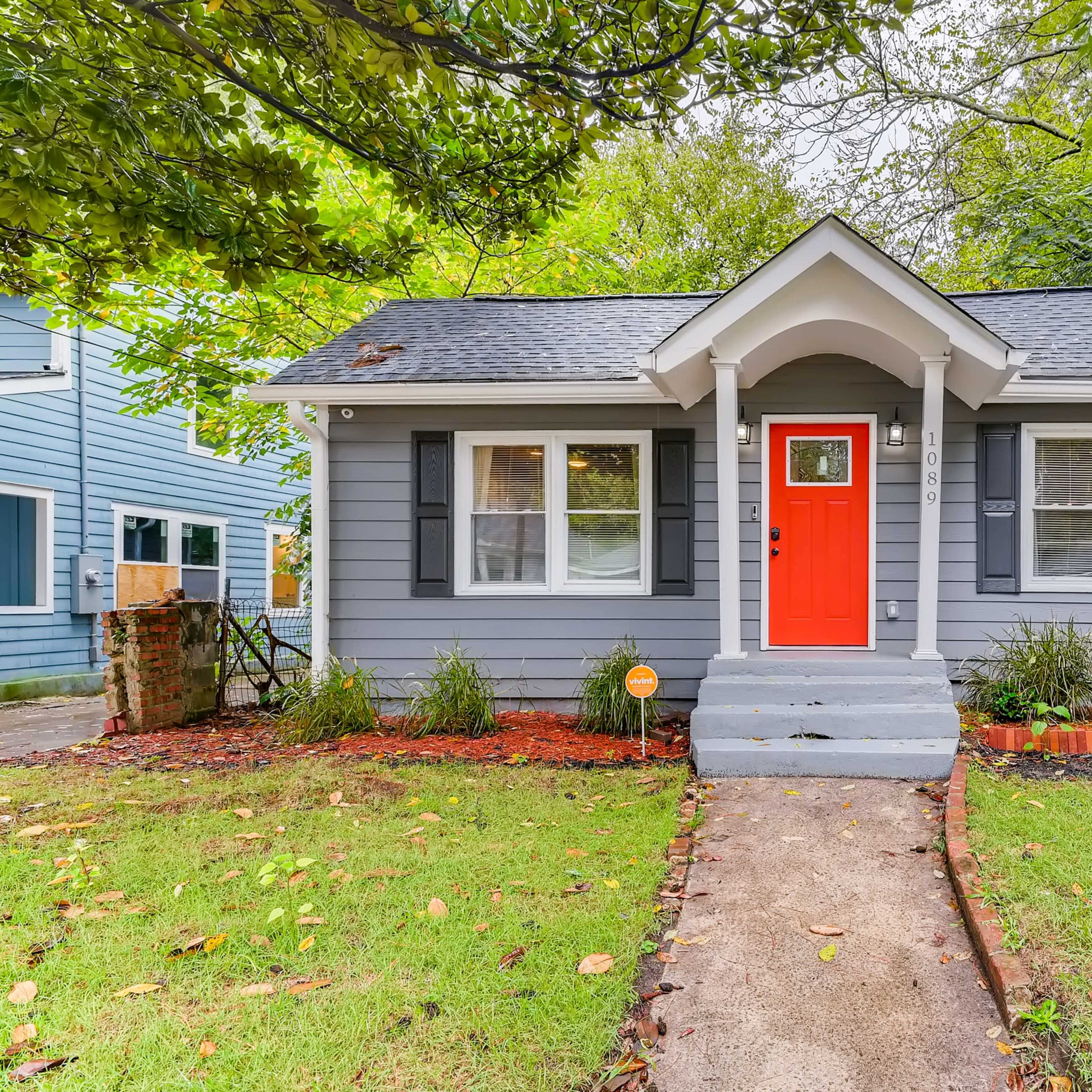 A small gray bungalow with a bright orange door and a well-maintained front yard.