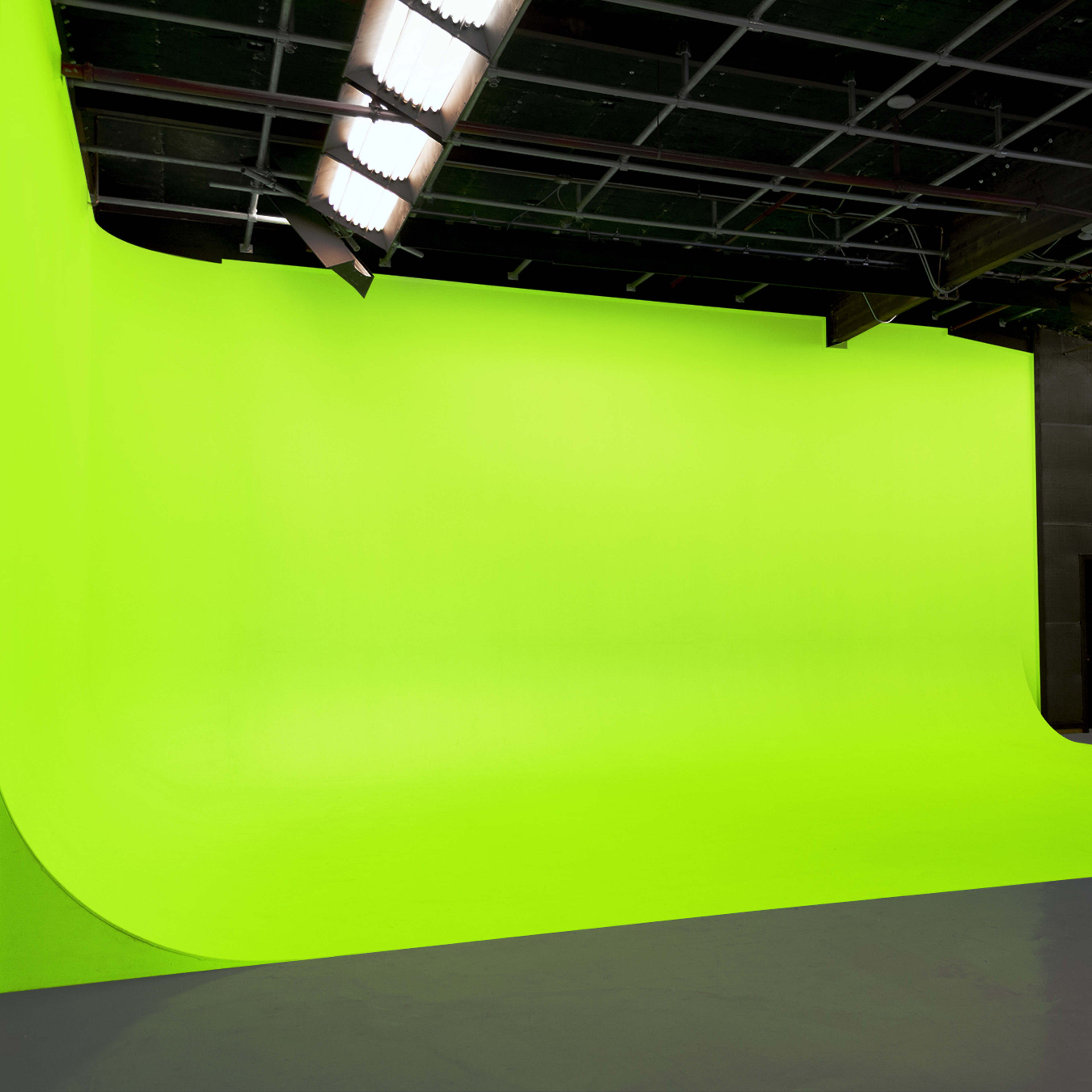 A spacious studio with a bright green screen background and gray flooring.
